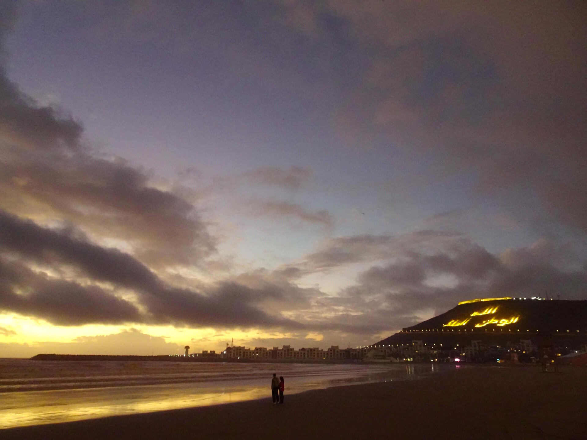 Agadir marina and fortress at sunset. Placing large writing on the side of hills seems to be very common in Morocco, this says 'God, Country, King'.
