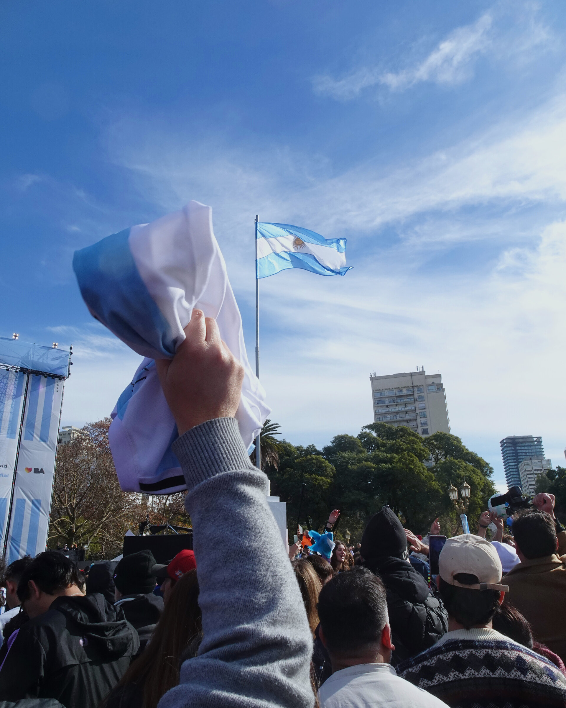 A raised hand waving a shirt in a crowd below the Argentine flag