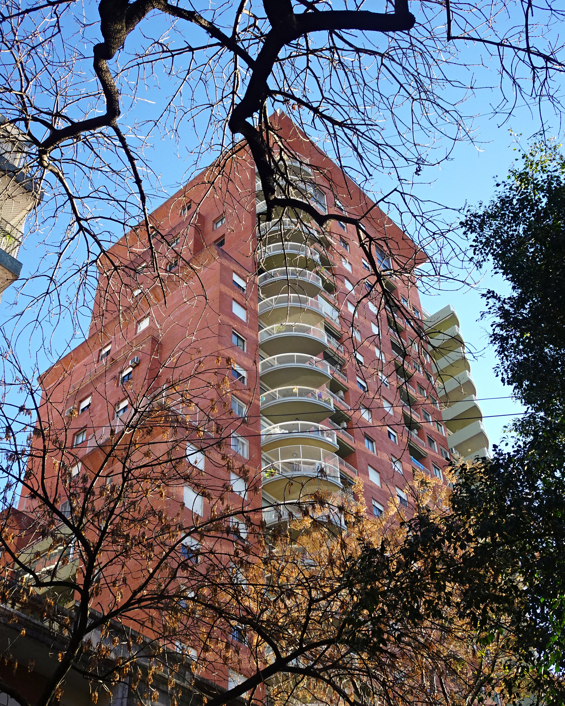 A red brick apartment block with curved balconies behind bare trees