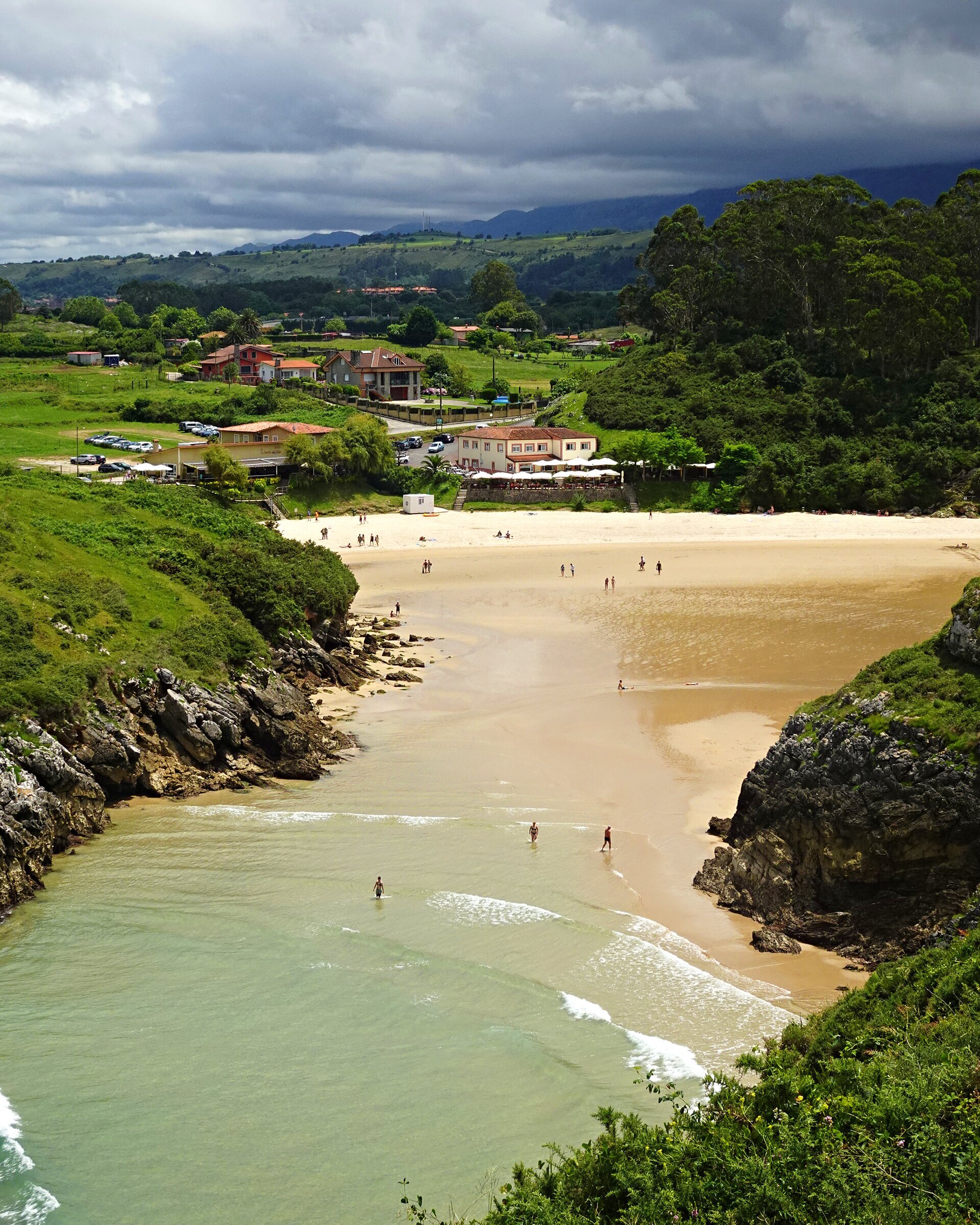 A sandy cove between green headlands with a village behind it
