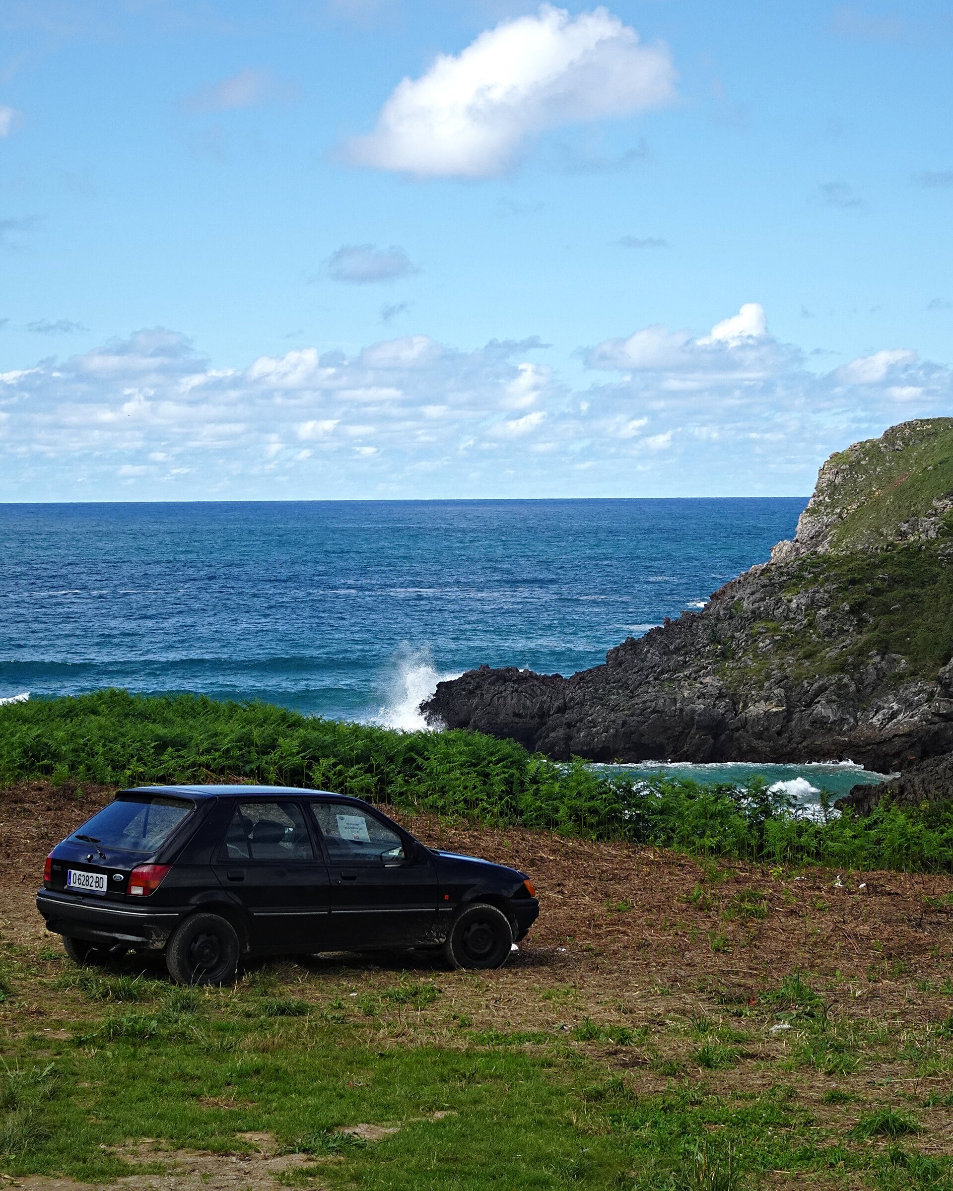 An old hatchback parked on a grassy clifftop above a breaking sea