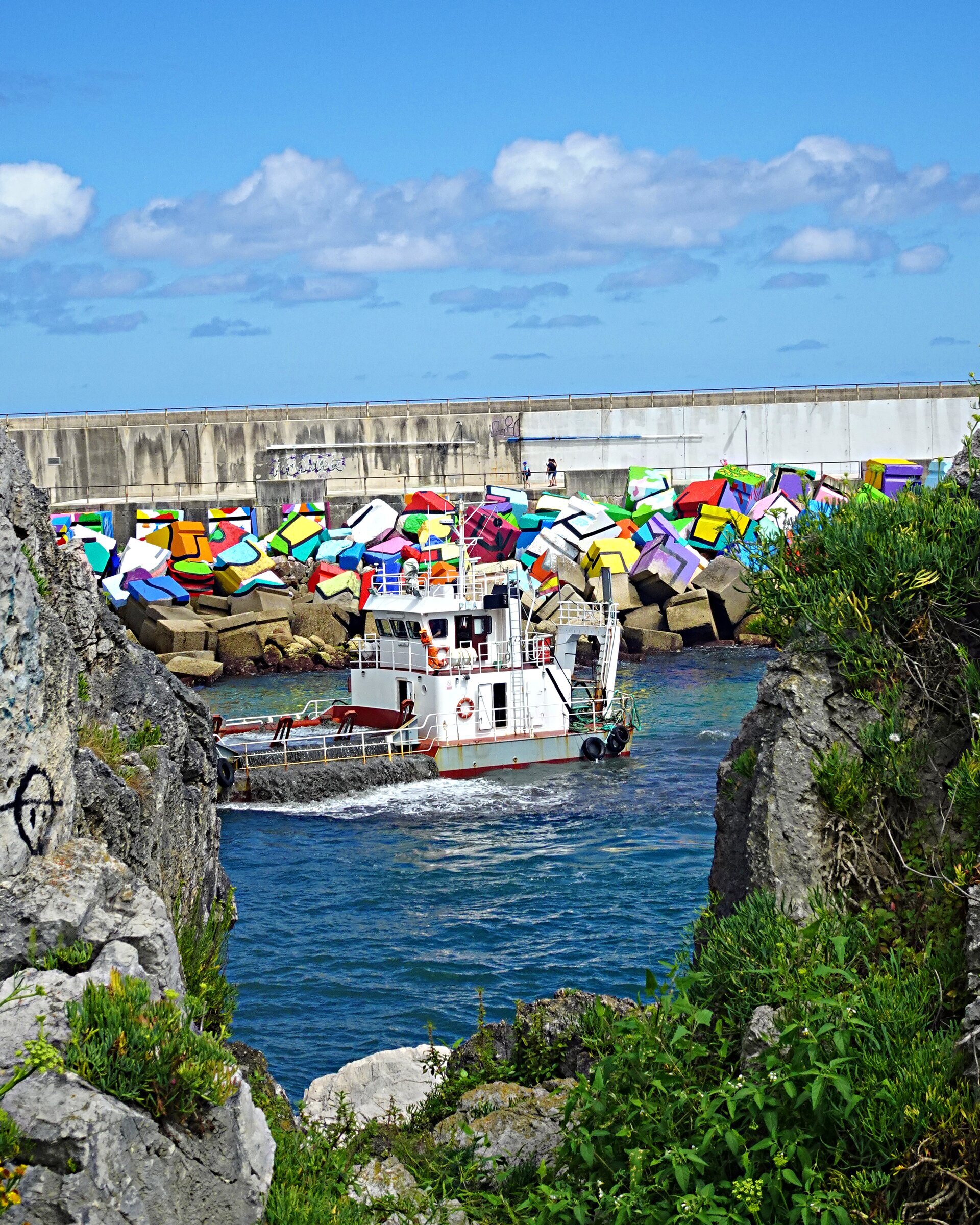 A boat passing a breakwater of brightly painted concrete blocks