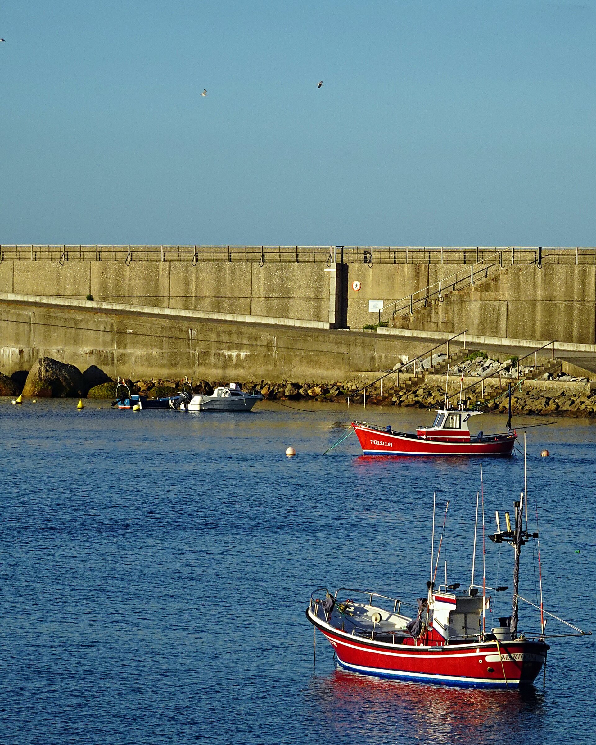 Two red fishing boats moored in still water below a harbour wall