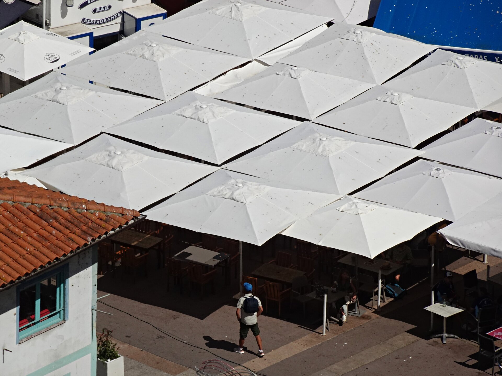 A man crossing a square beneath a grid of white café umbrellas
