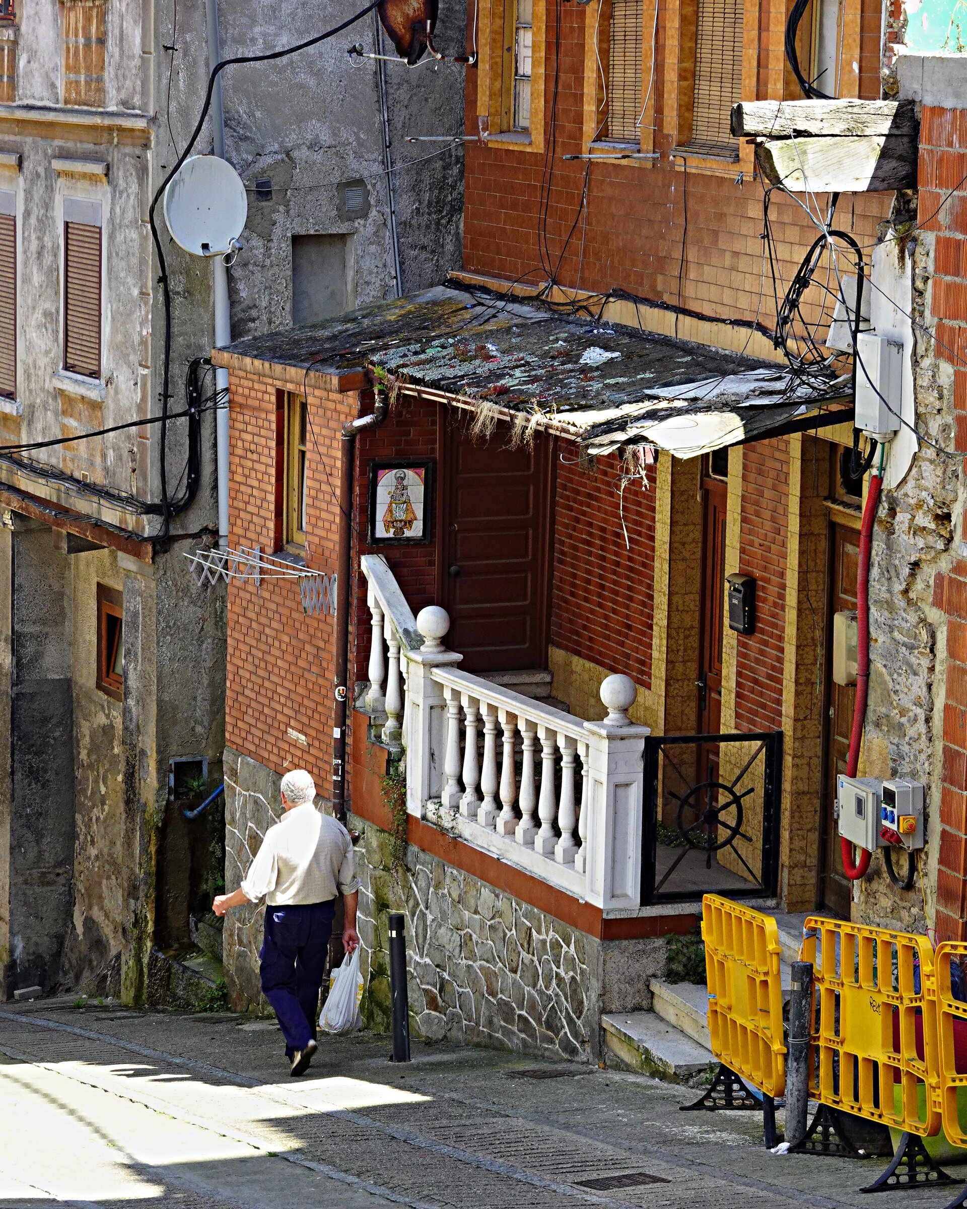 A man carrying shopping up a narrow street of tangled cables
