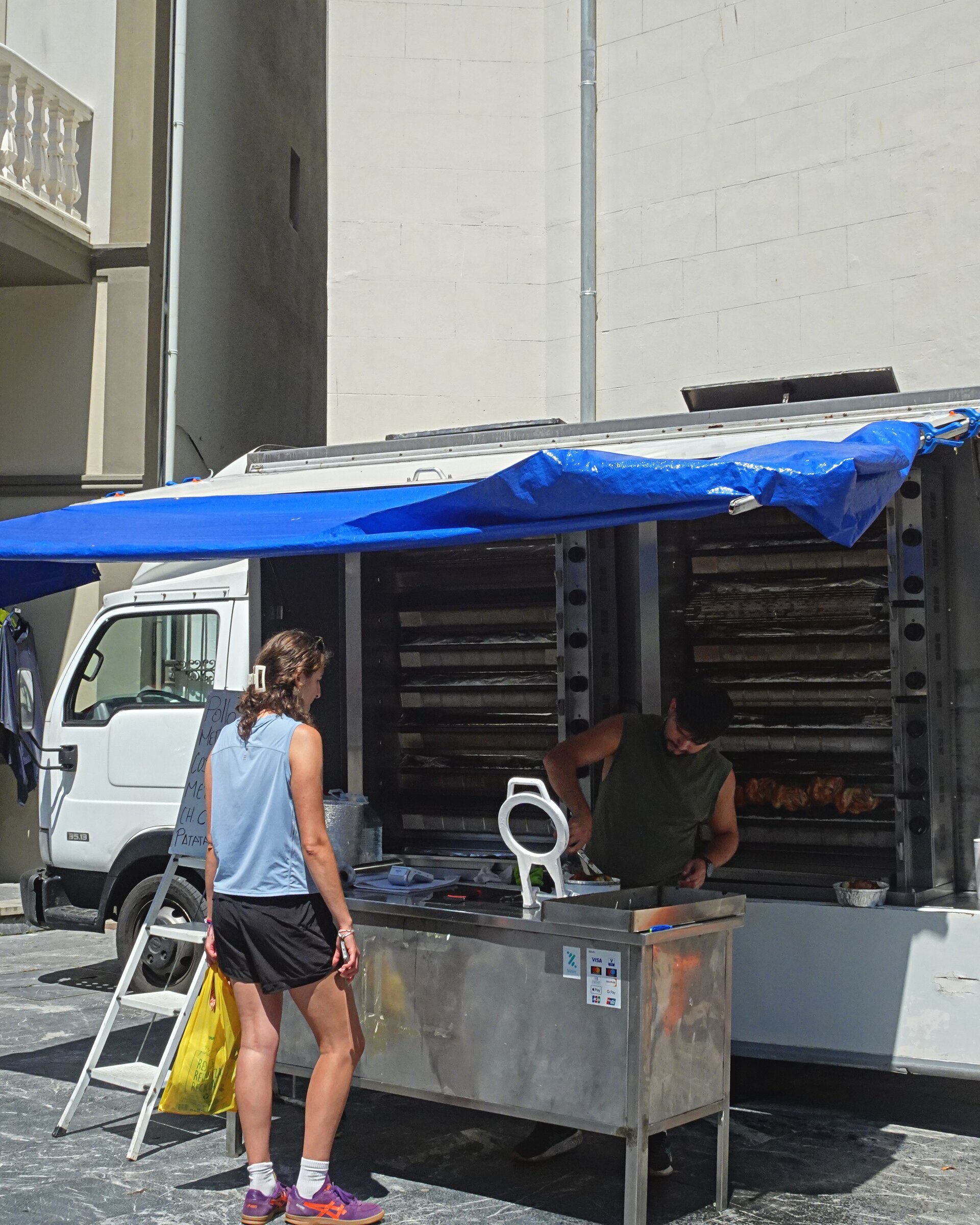 A woman waiting at a rotisserie chicken van parked in a square