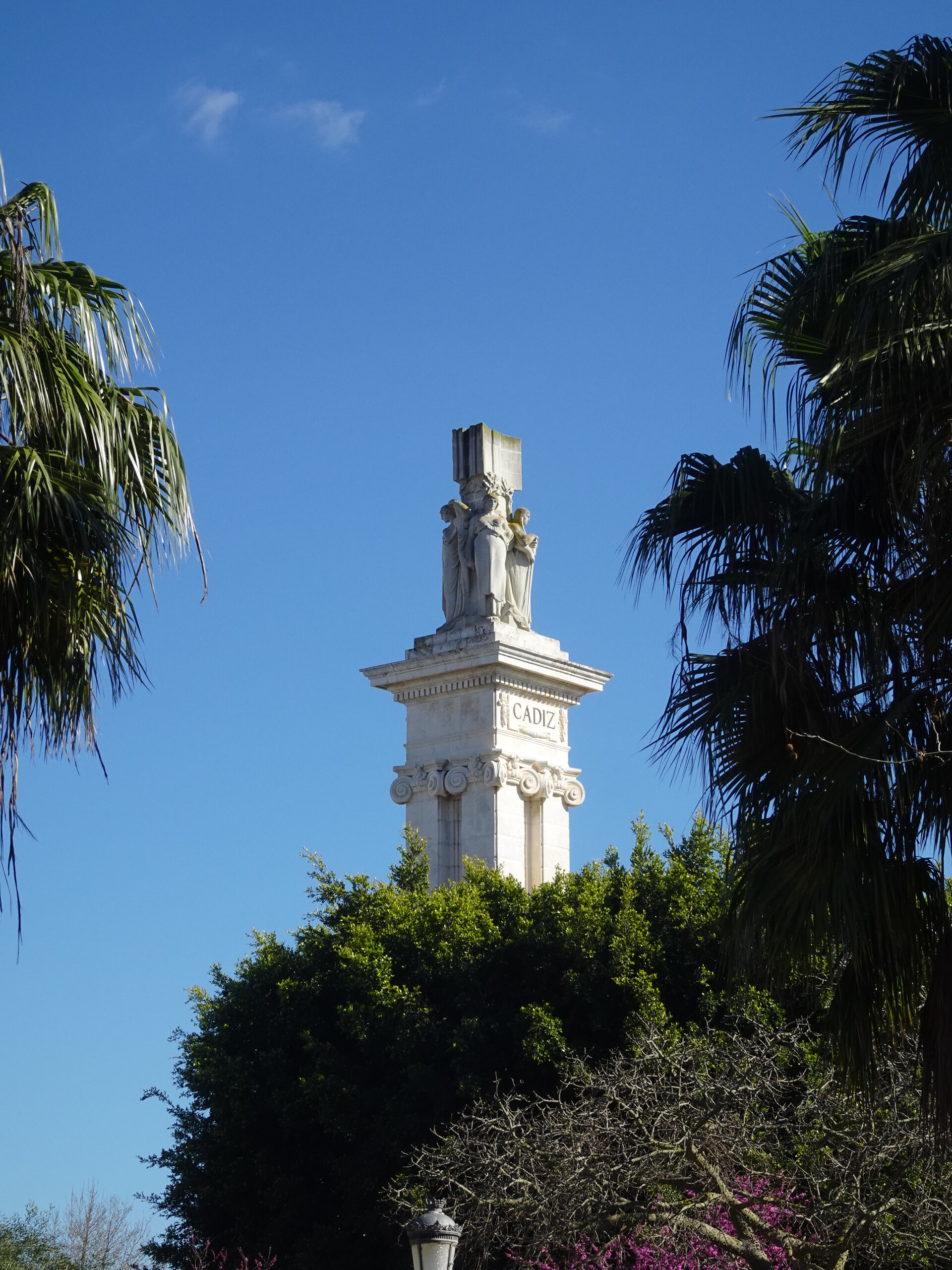 Cadiz monument rising above palm trees and gardens