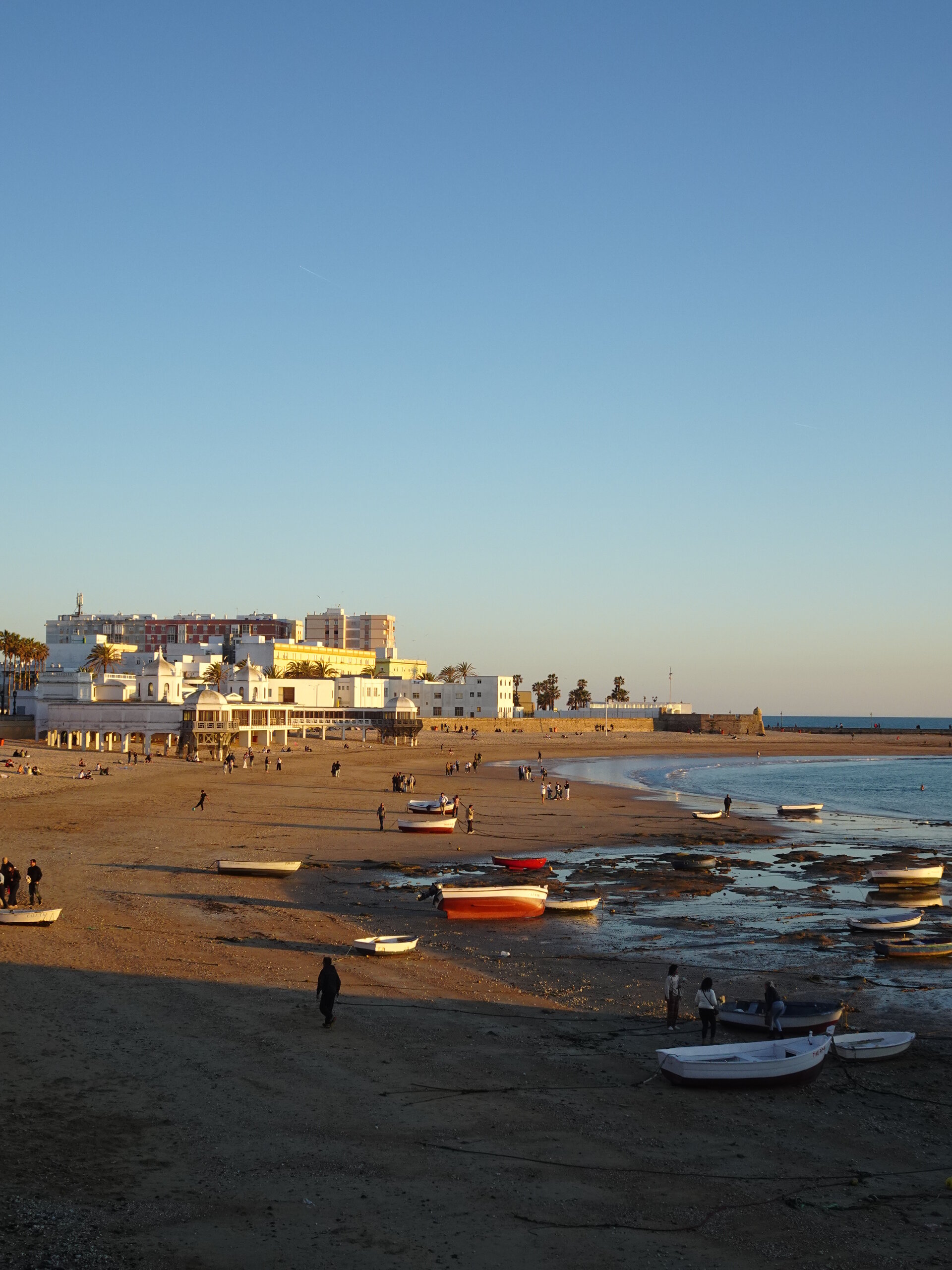 Small boats on a beach at golden hour with white buildings