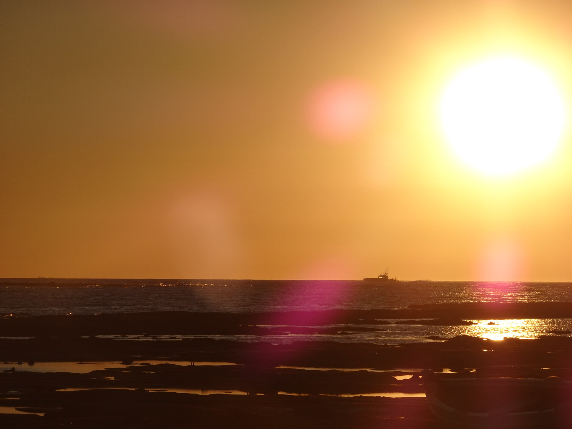 Sunset over the sea with a ship silhouetted on the horizon