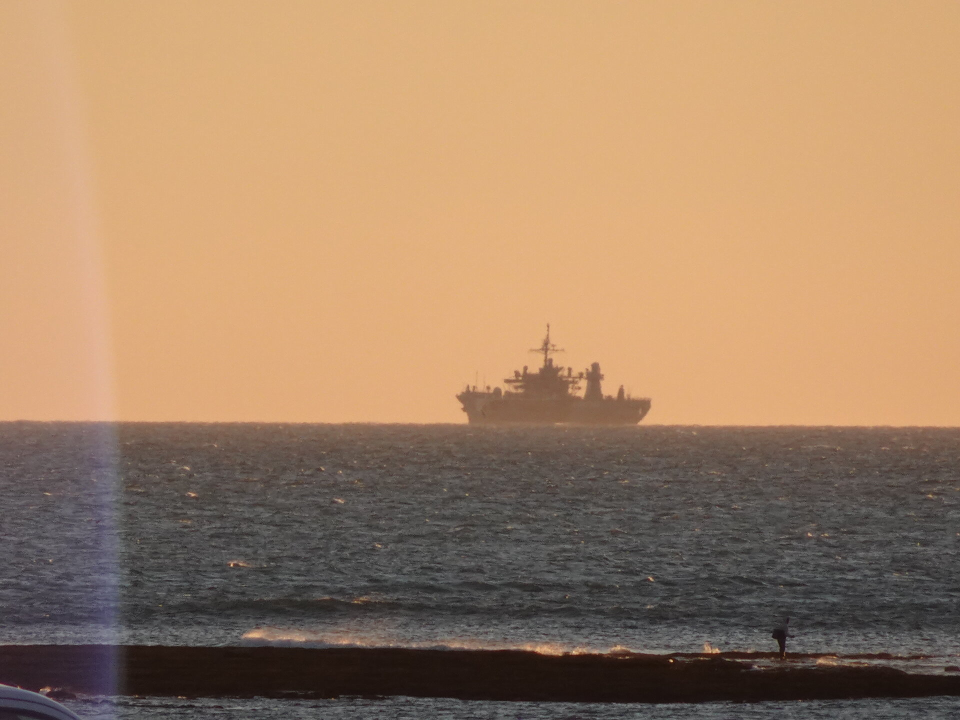 Military ship silhouetted against a golden sunset sky
