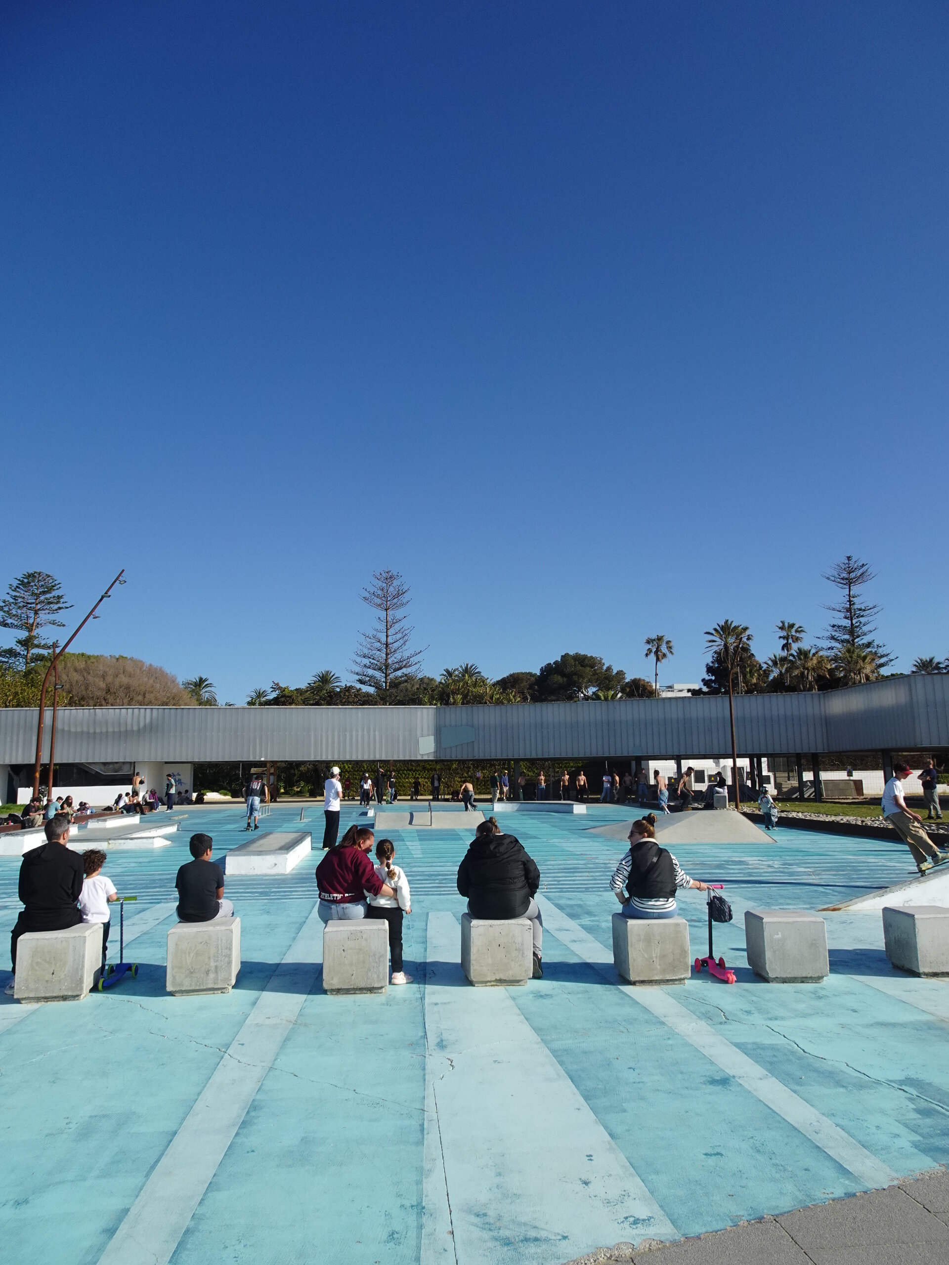 People sitting watching skaters at a blue skatepark