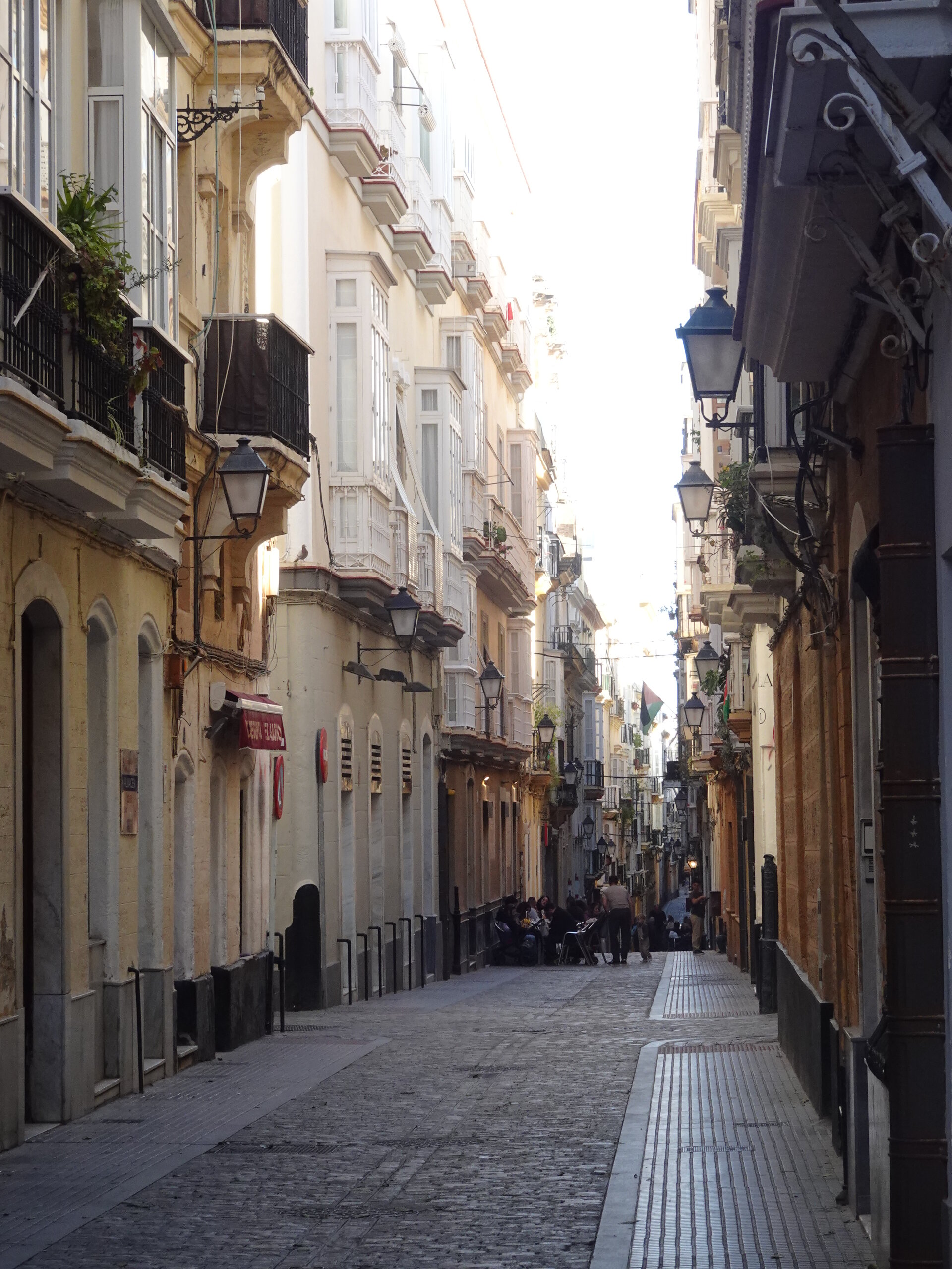 Narrow sunlit cobblestone street with balconies and lanterns