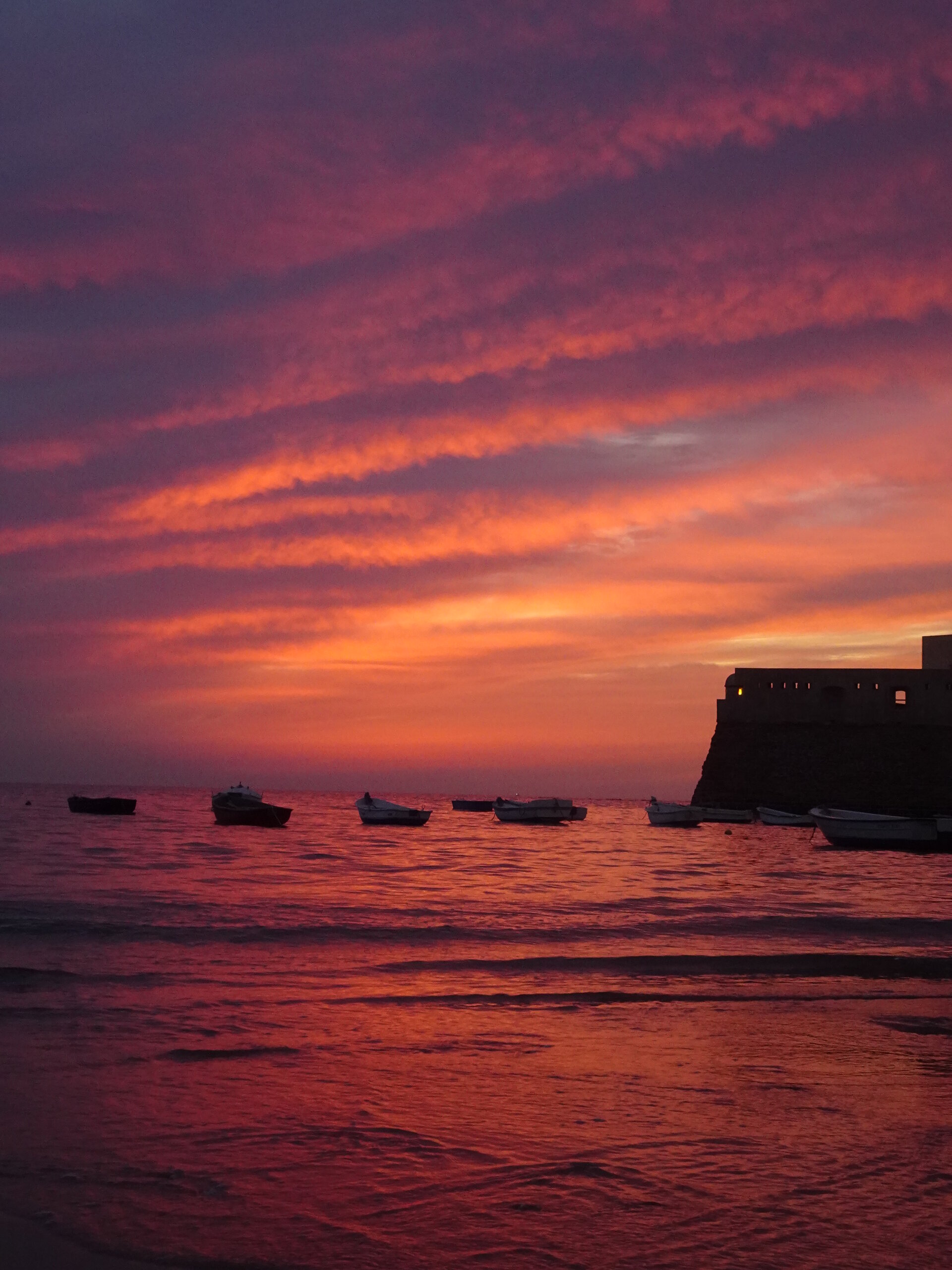 Boats and a fortress silhouetted against a vivid red sunset