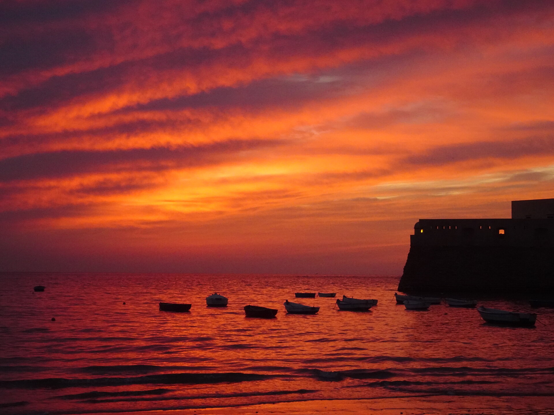 Fiery orange and red sunset over boats and a sea fortress
