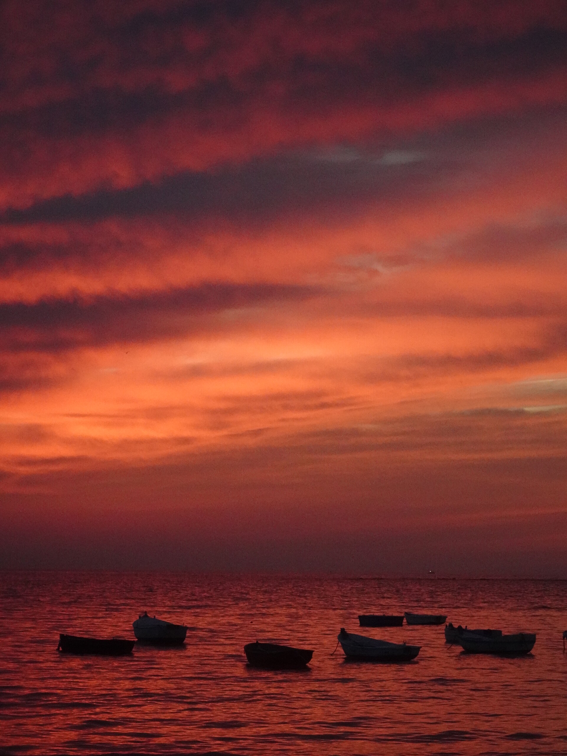 Boats silhouetted under a deep crimson sunset sky