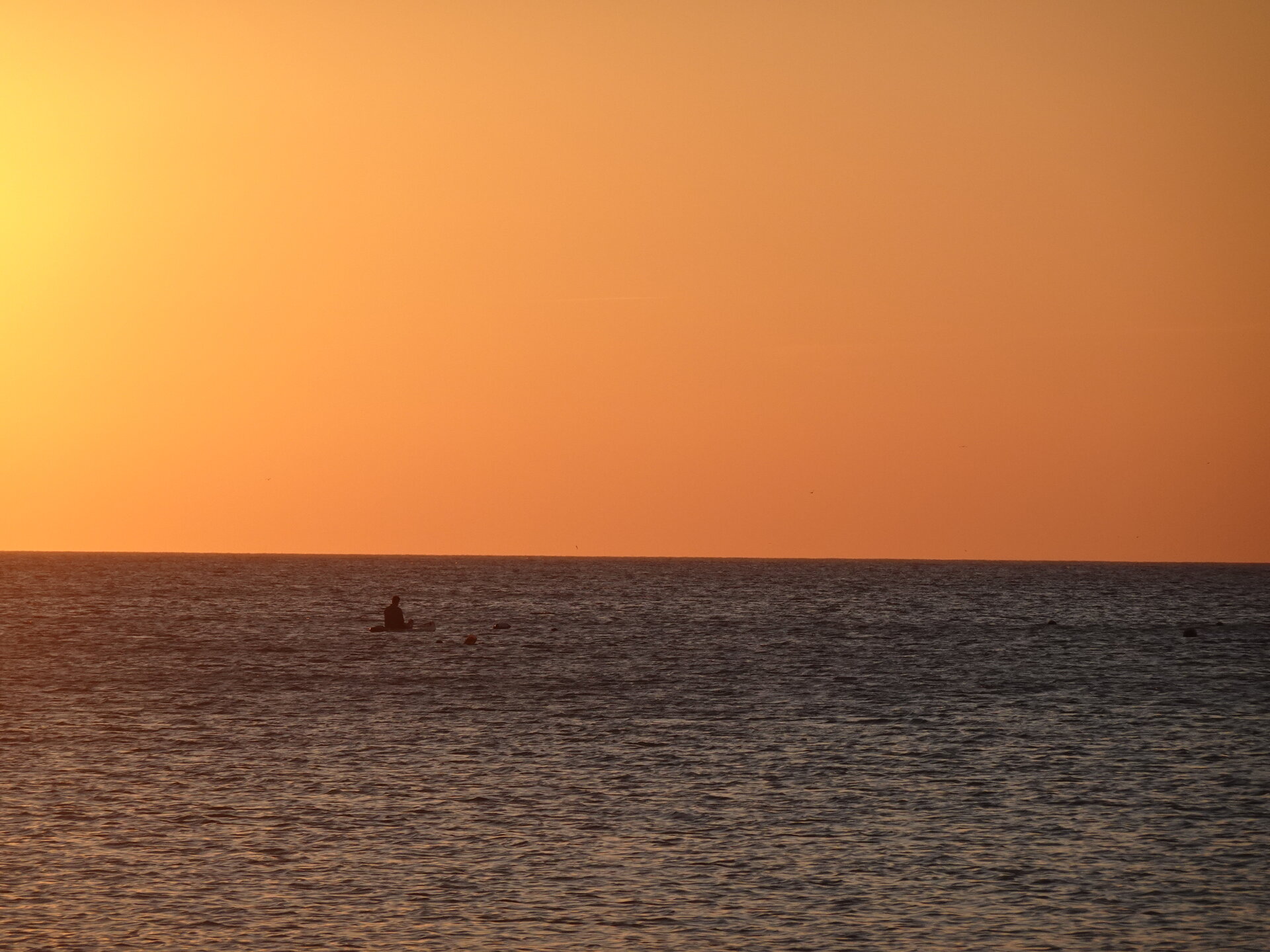 Calm orange sea at sunset with a kayaker on the horizon