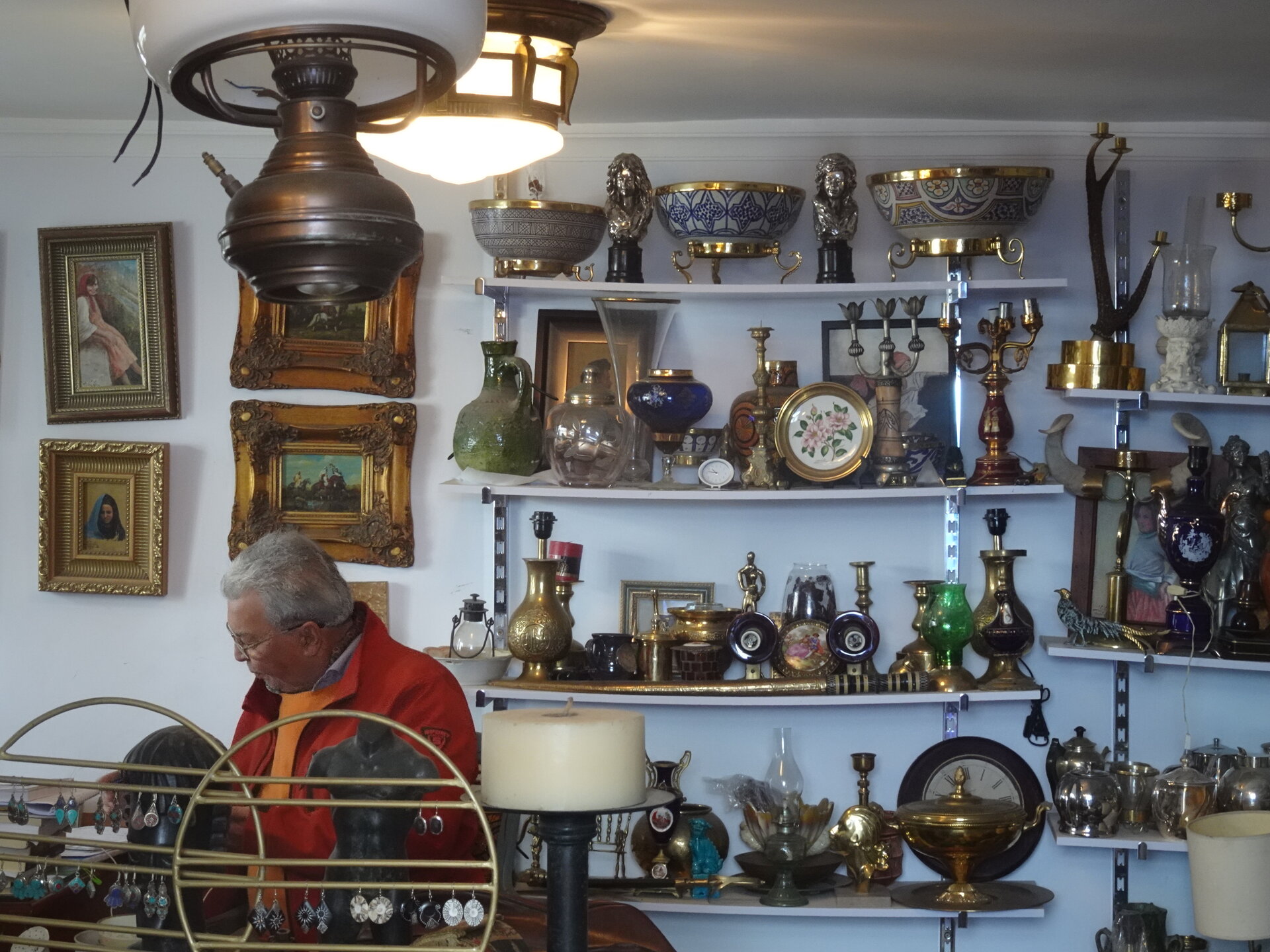 Man working in an antique shop filled with brass lamps and glassware