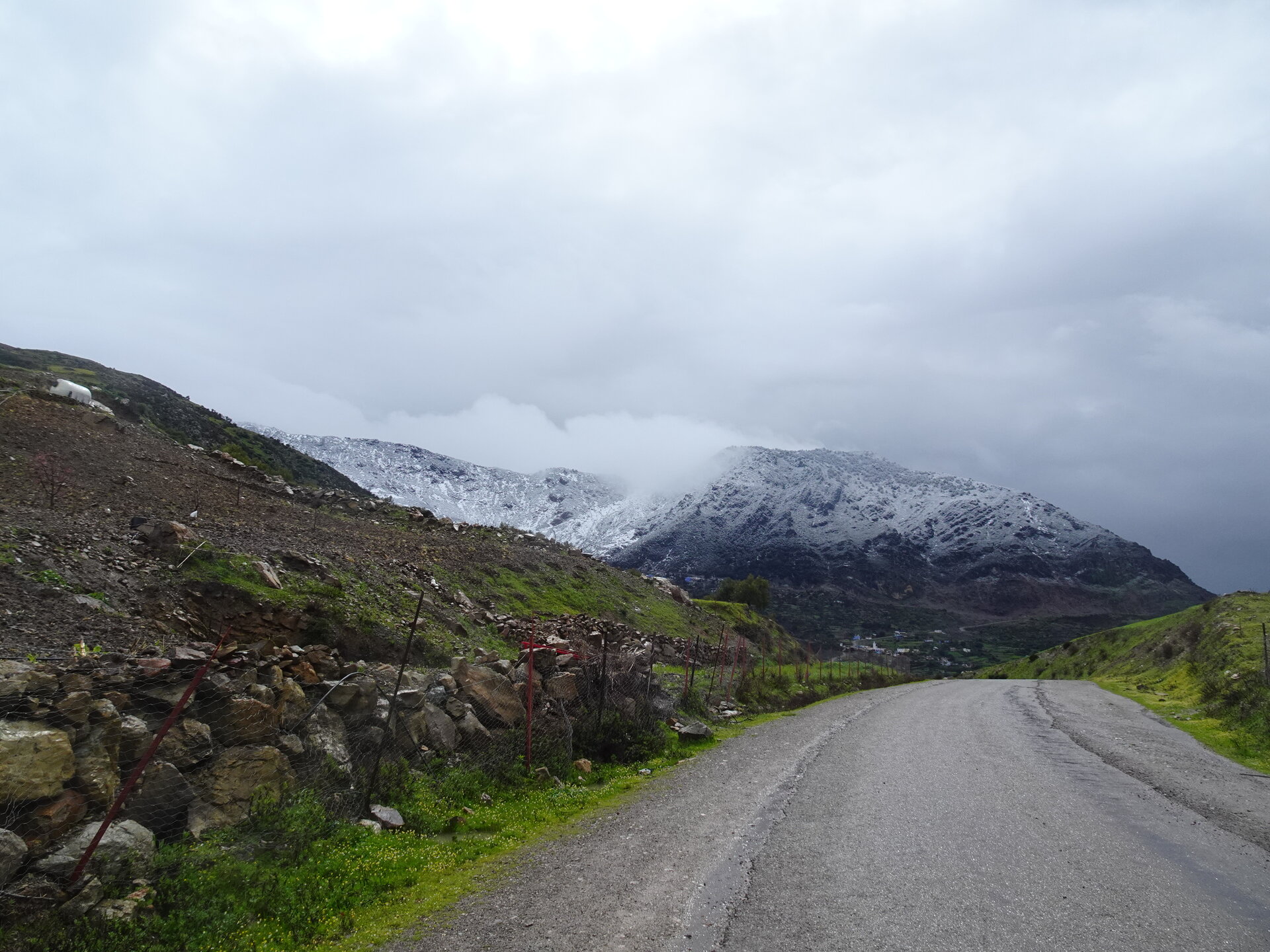Mountain road curving toward snow-covered peaks under heavy cloud