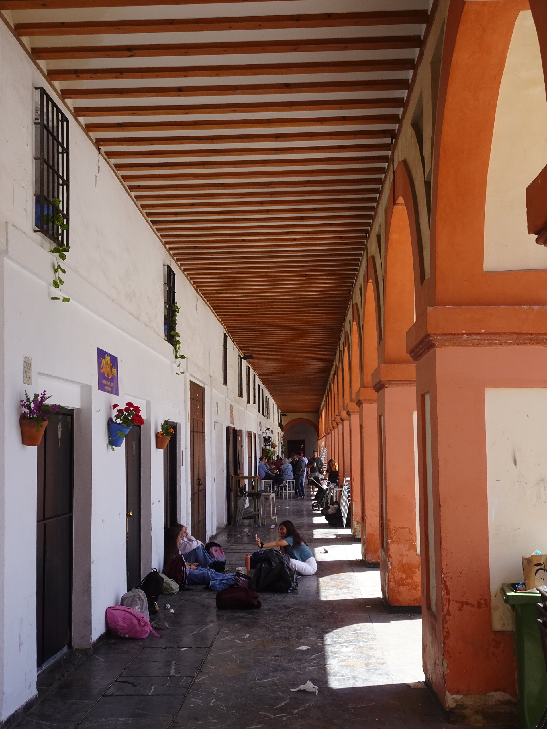 Long arcaded loggia with red columns and people resting in the shade