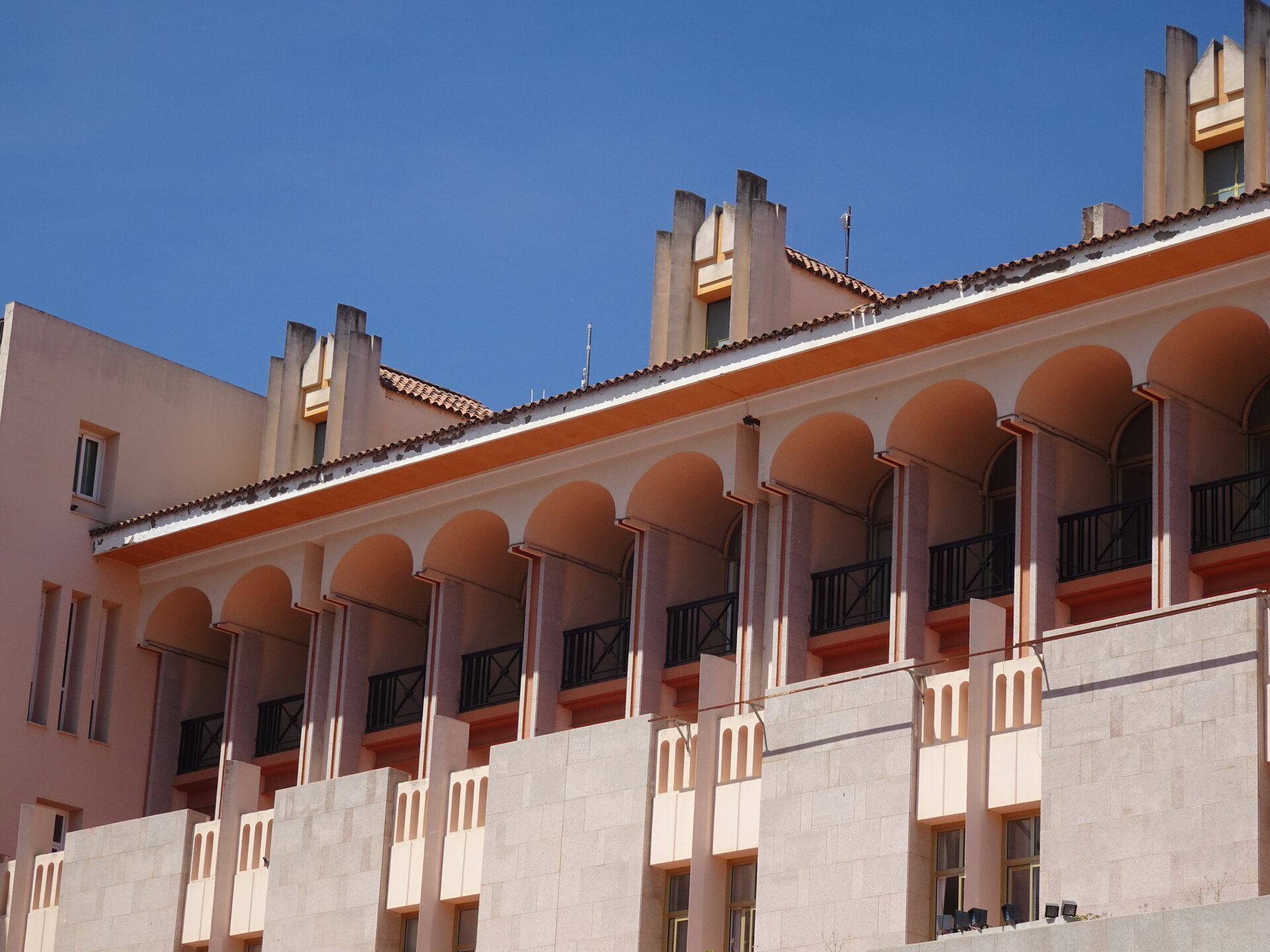 Pink Andalusian building with arched colonnade and crenellated parapet