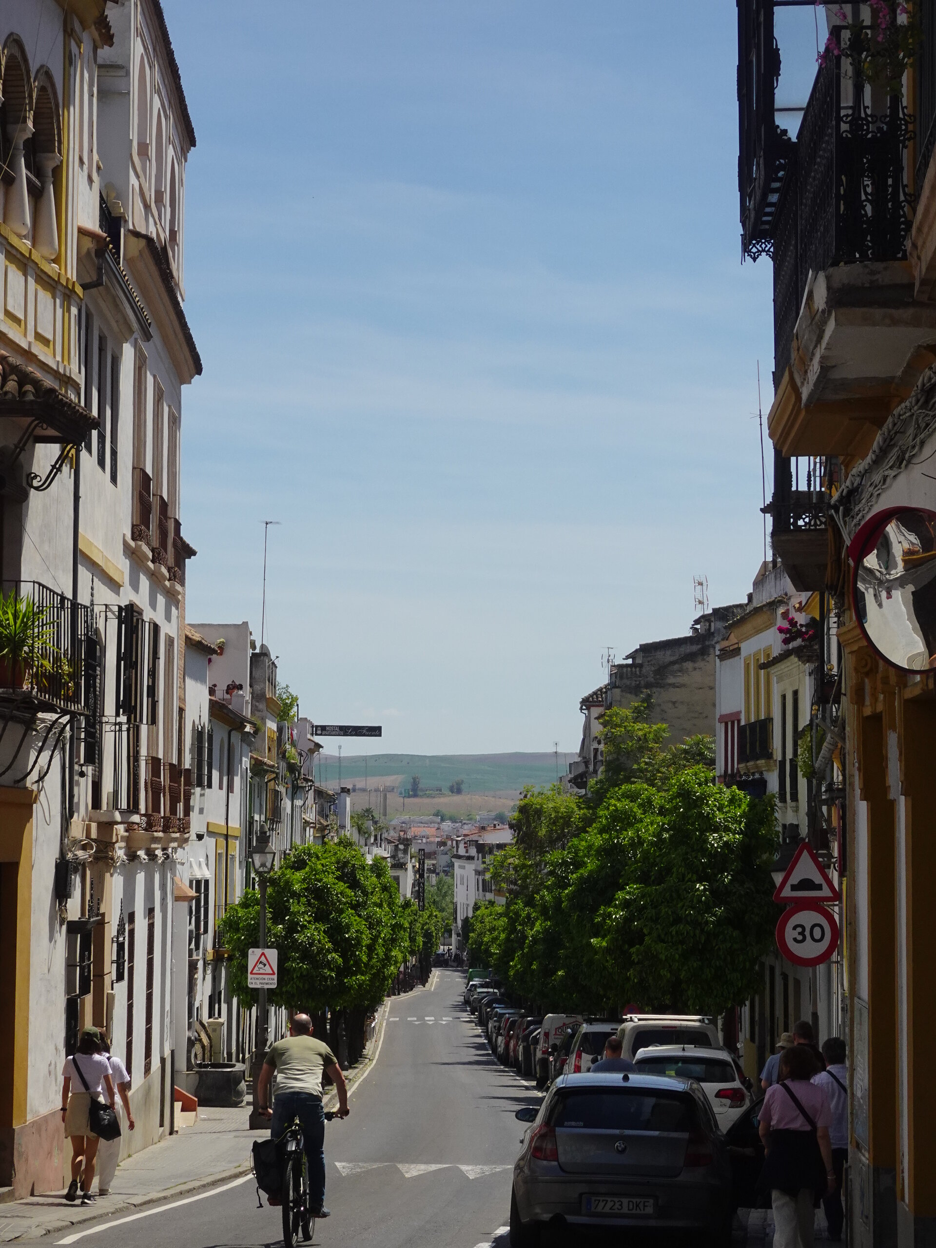 Long city street dropping toward distant countryside with a cyclist riding away
