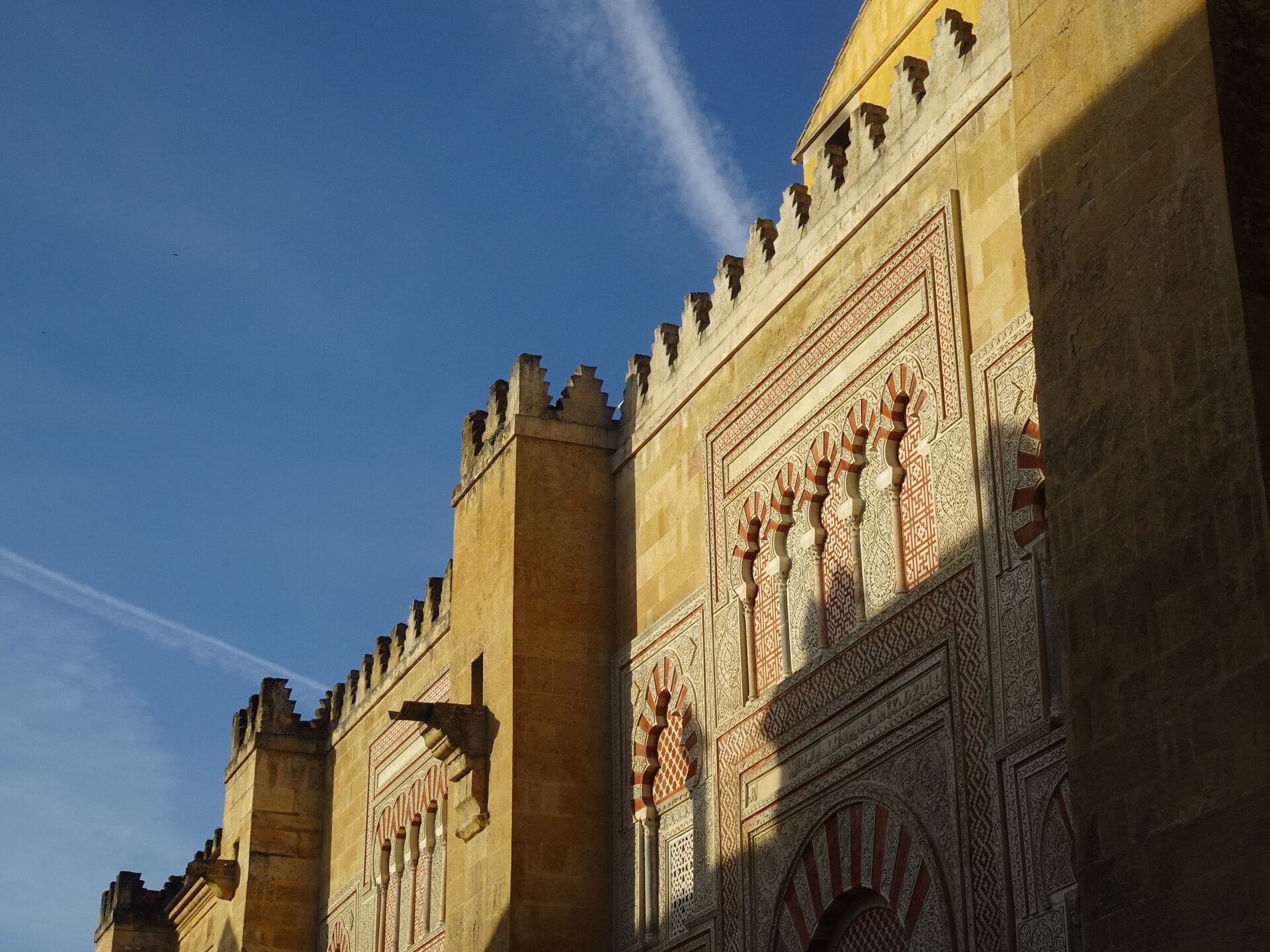 Exterior wall of the Mezquita with intricate horseshoe arch carving against blue sky
