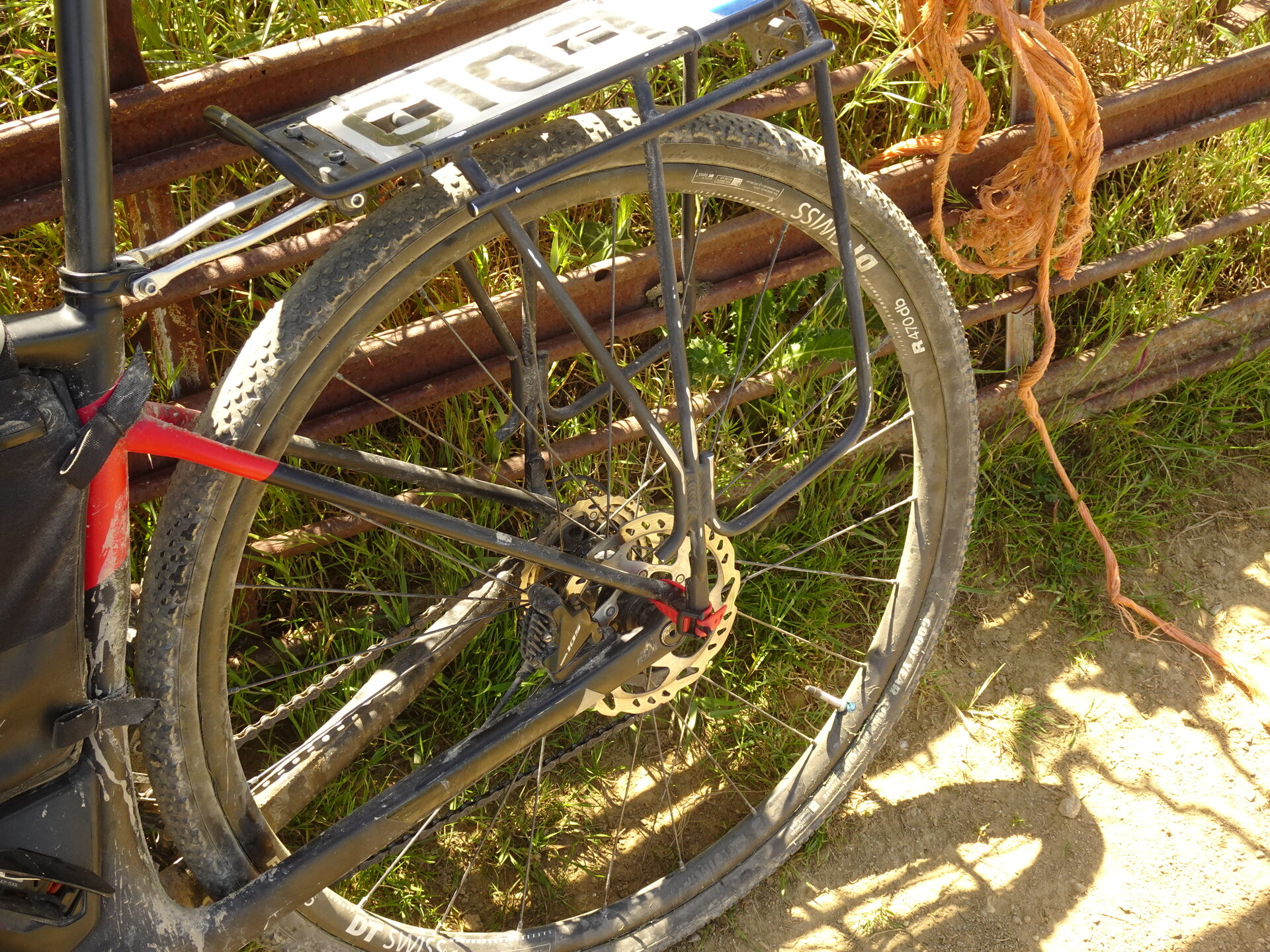 Rear wheel of a loaded touring bike leaning against a rusted metal gate