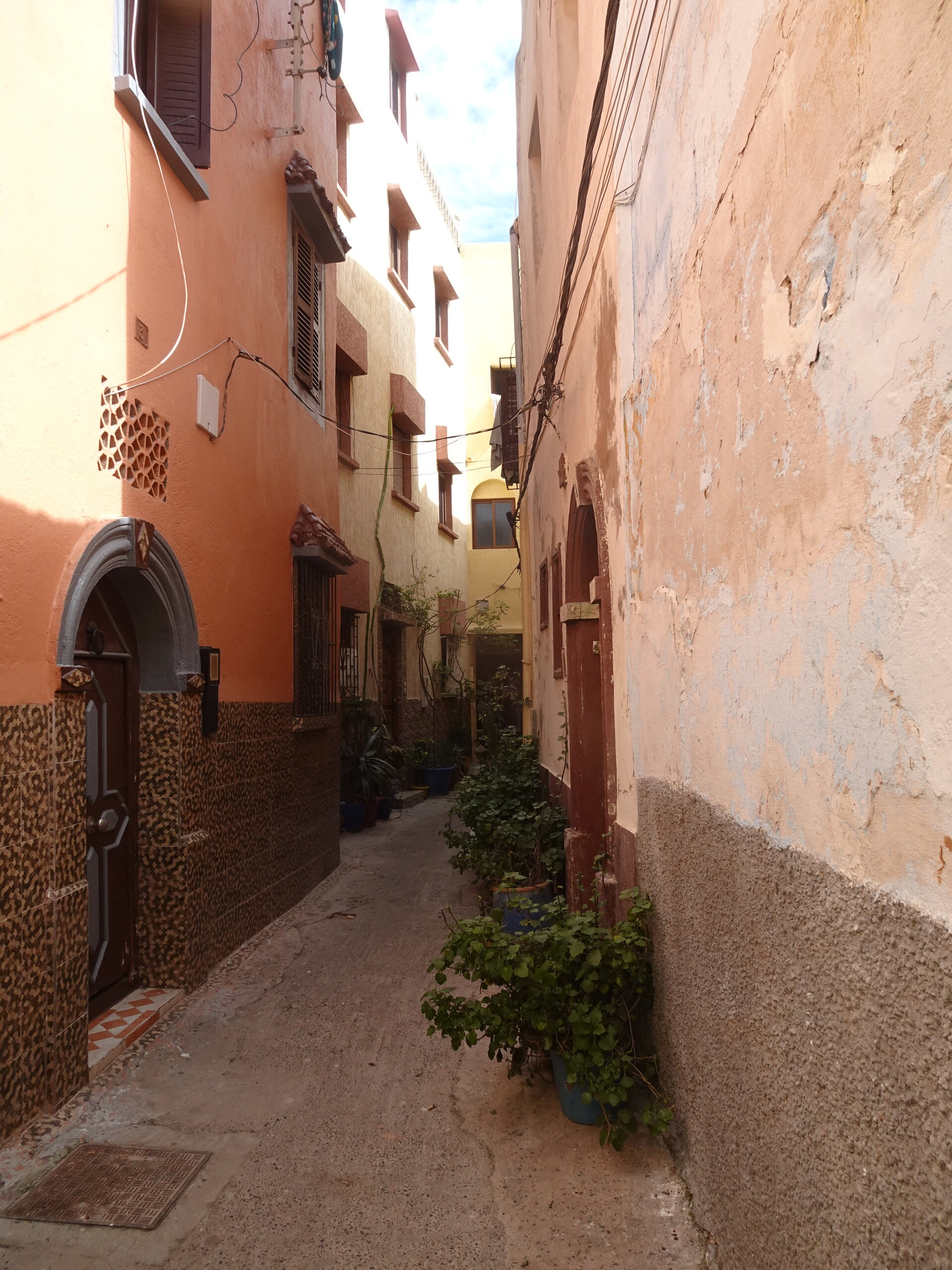 Narrow orange and terracotta alley with an arched doorway and potted plants
