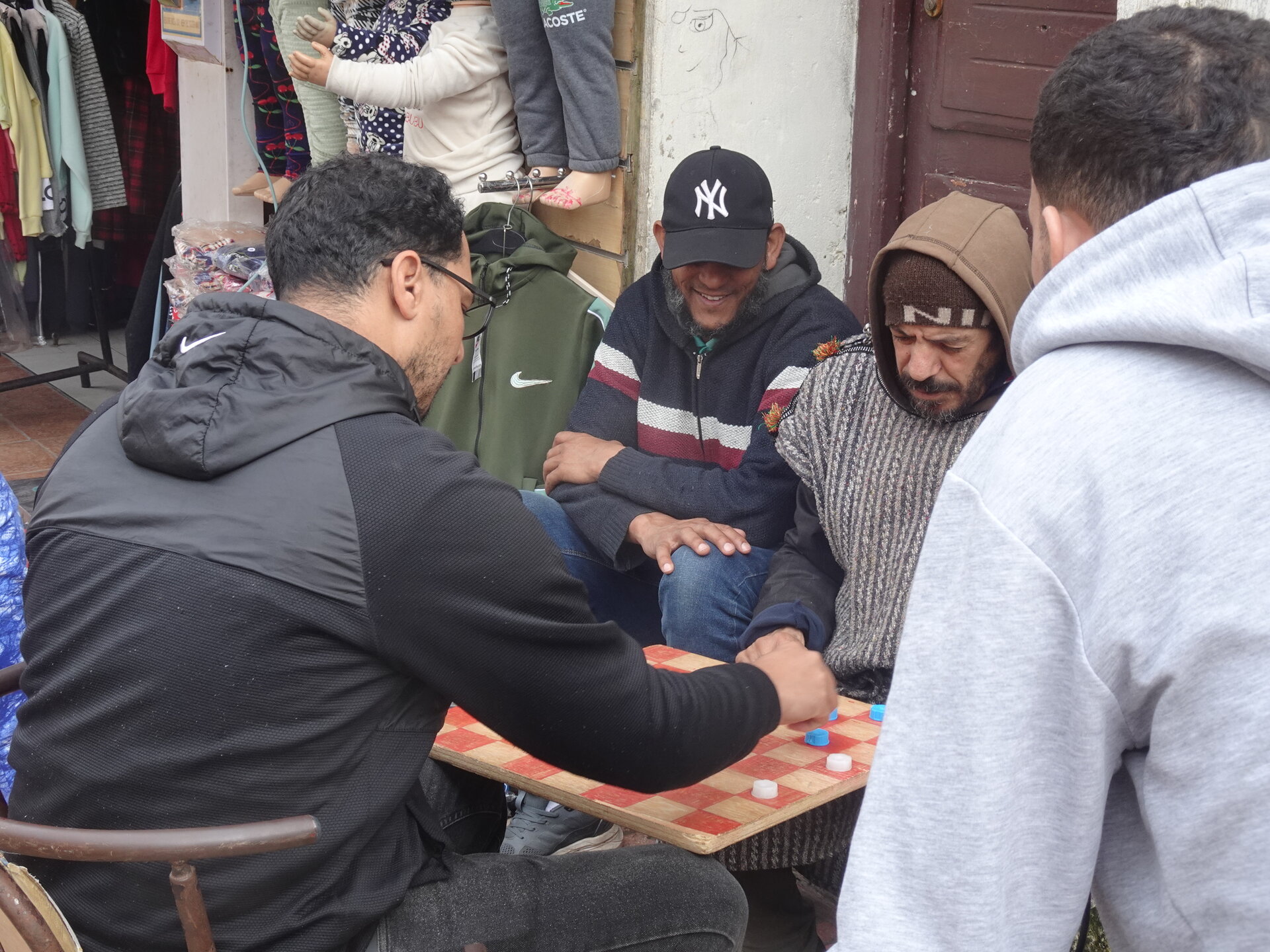 Group of men playing checkers on the street outside a clothing shop