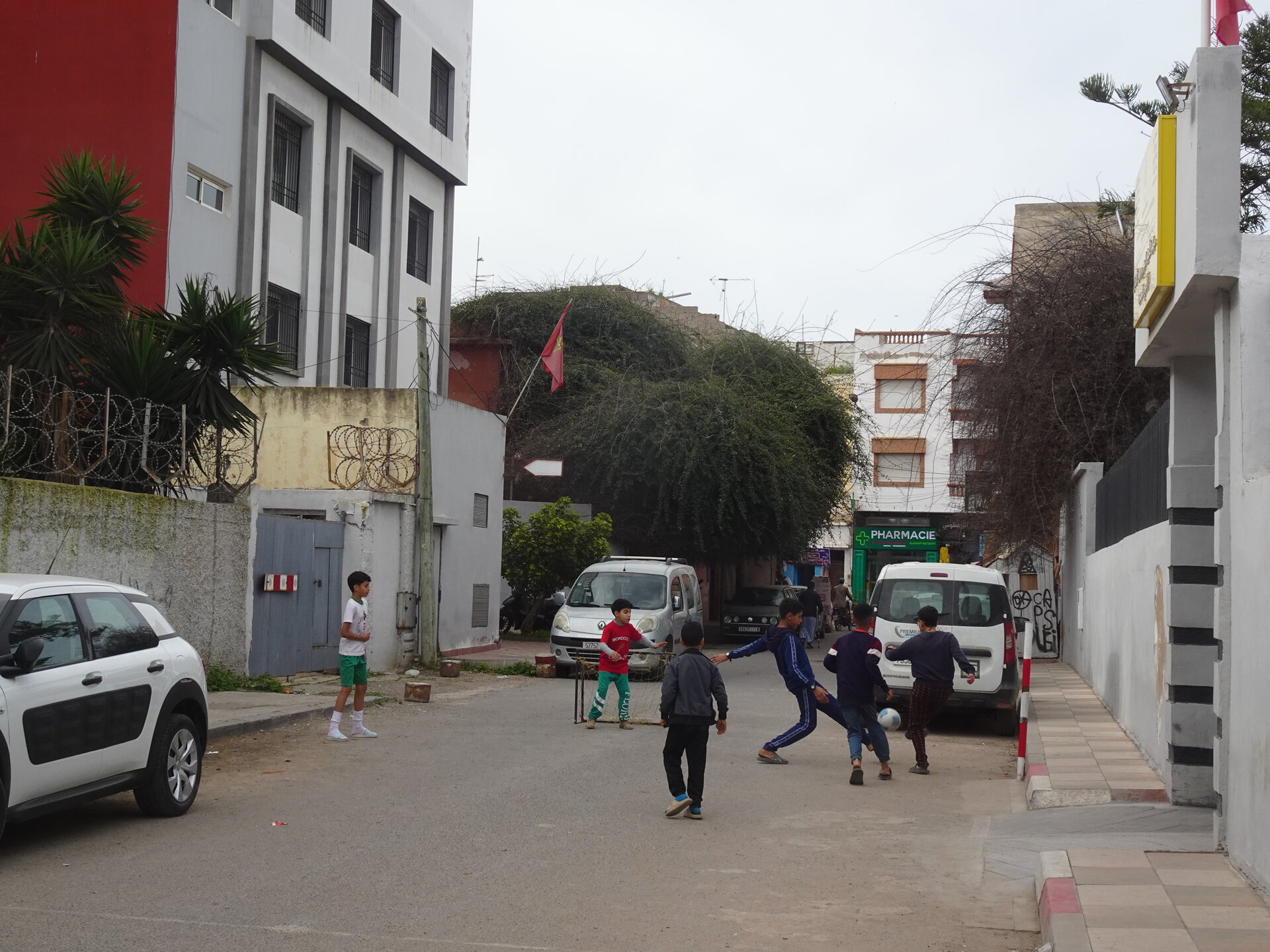 Kids playing football in a side street with a pharmacy and Moroccan flag in the background