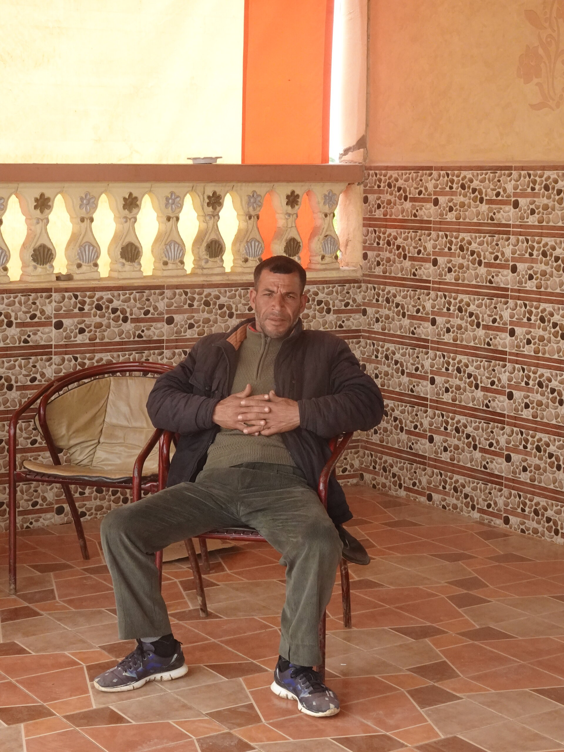 Man seated in a tiled porch with hands clasped