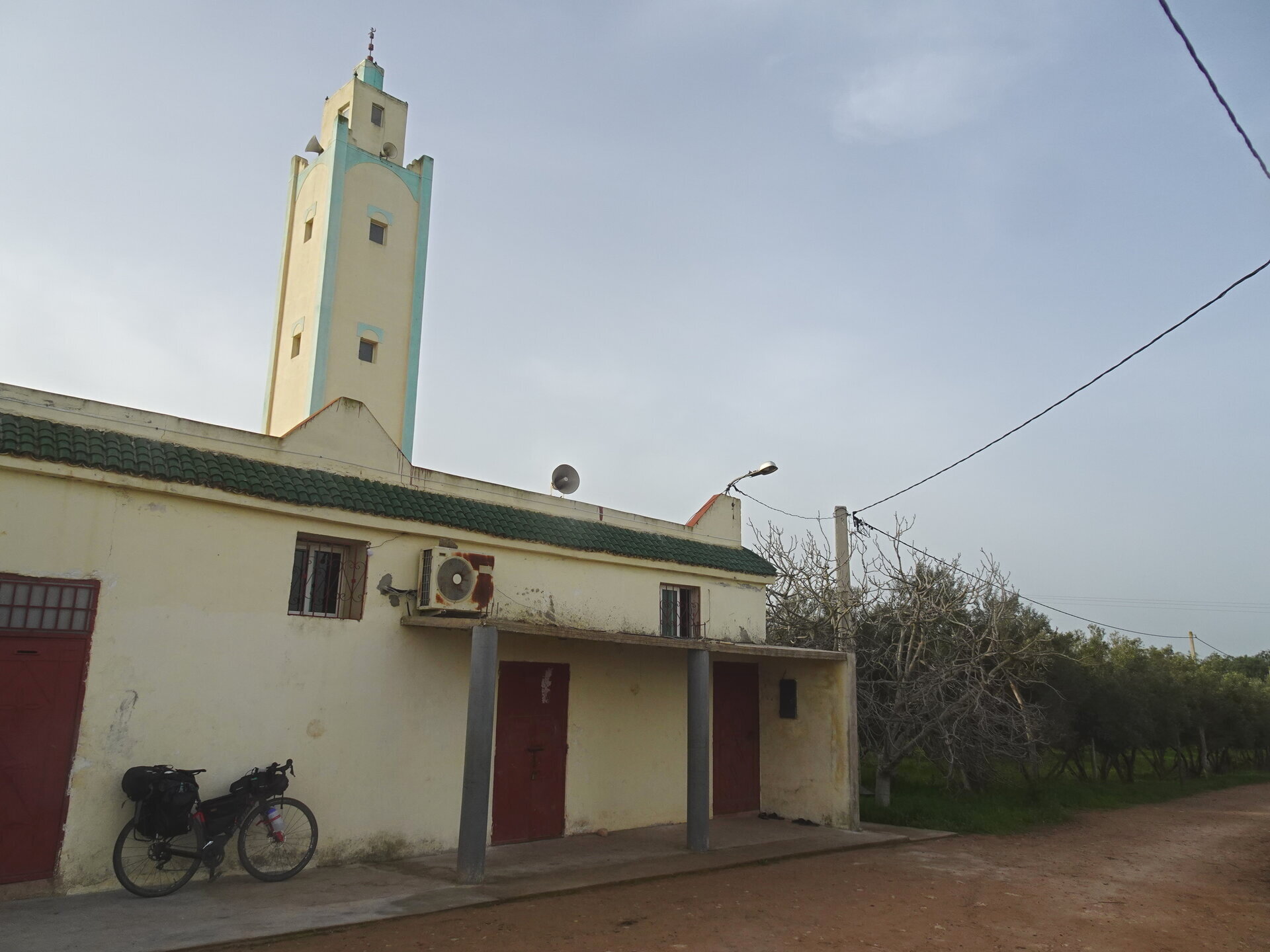 Bike parked outside a small mosque with a green and white minaret