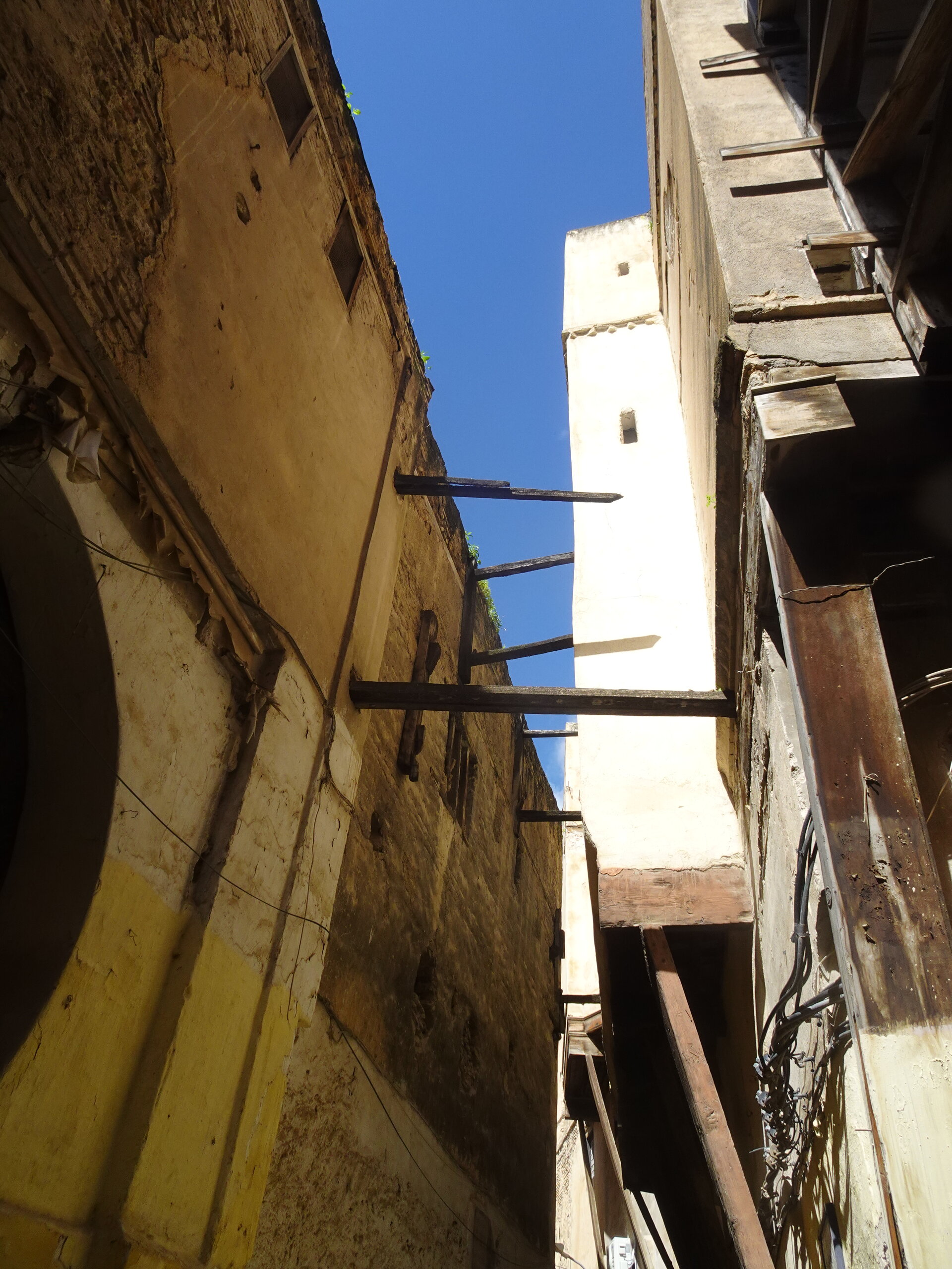 Tall medina buildings with wooden braces spanning a narrow gap of blue sky