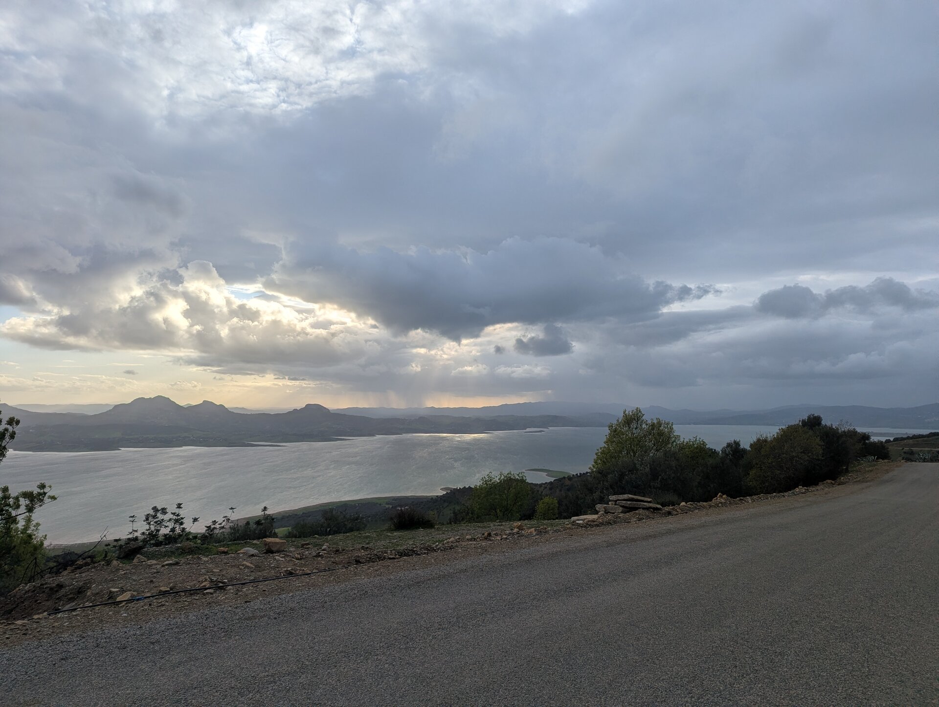 Road overlooking a lake at dusk with storm clouds and distant rain