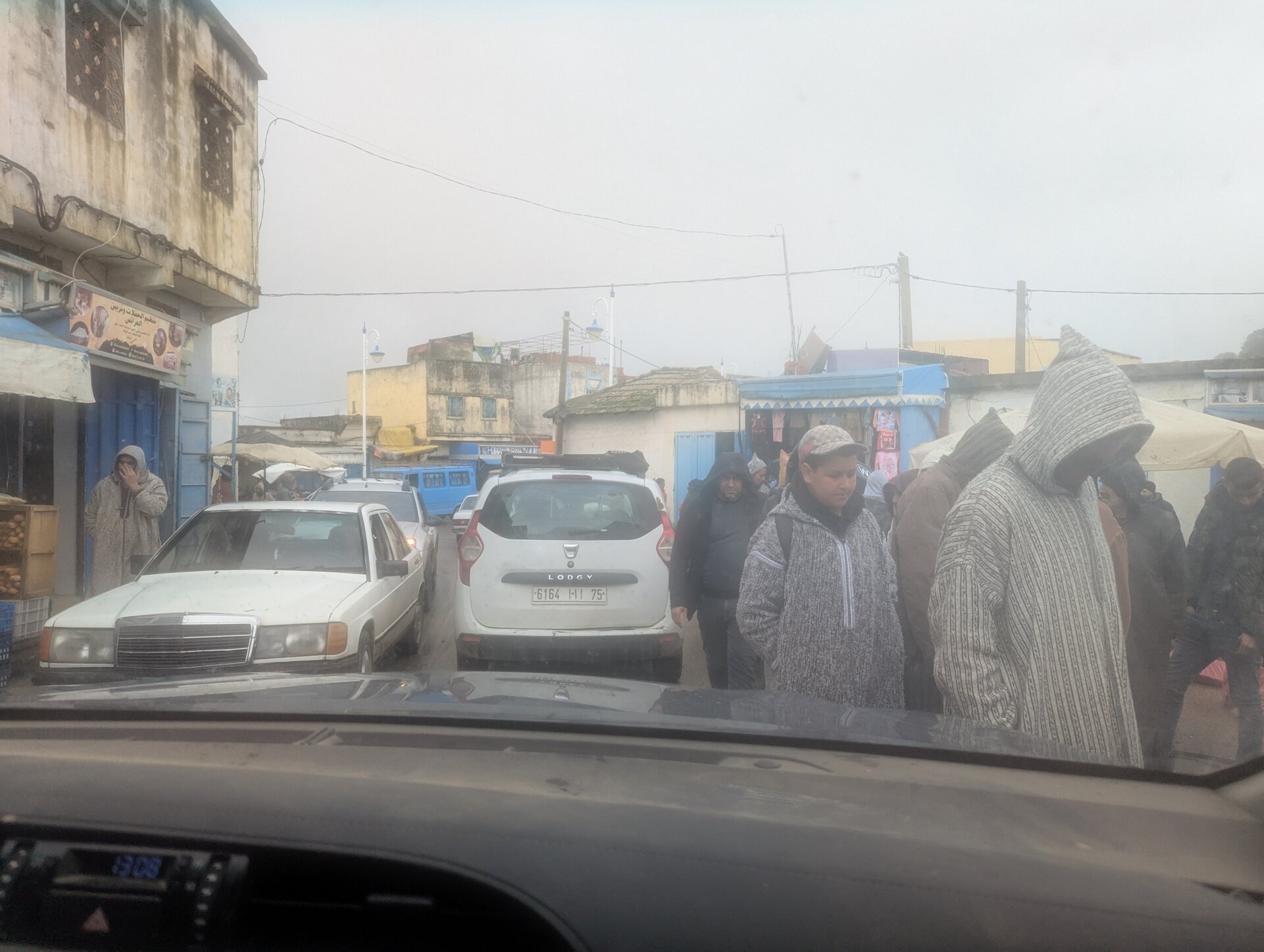 Foggy town street crowded with cars and people in hooded jackets