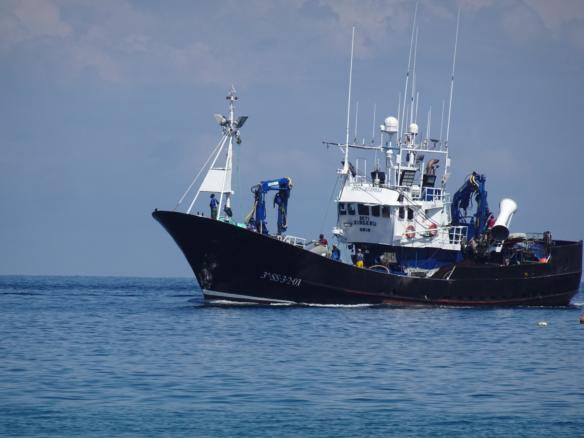 Black-hulled fishing trawler underway on a calm blue sea