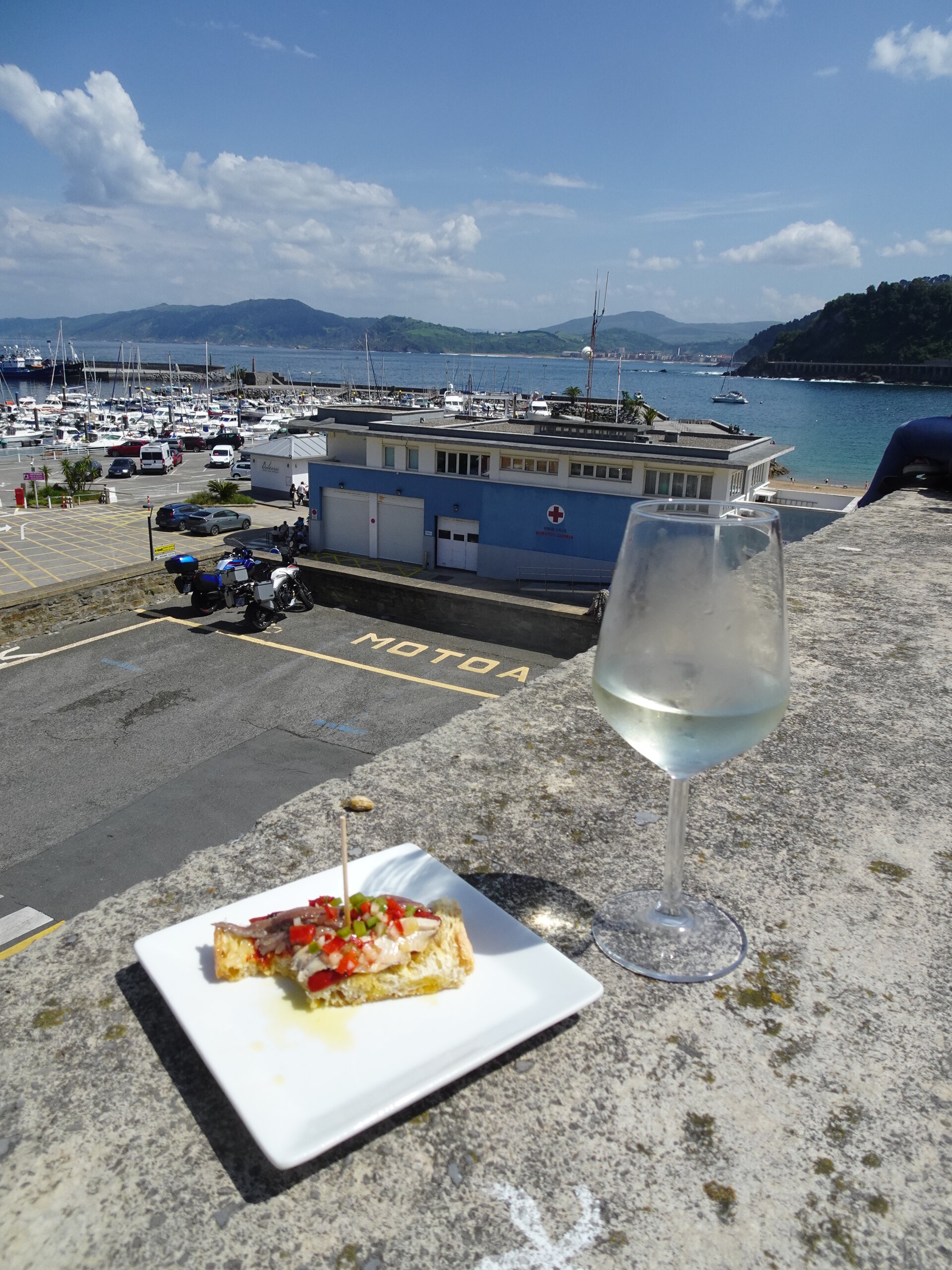 Glass of white wine and a pintxo on a plate overlooking a marina