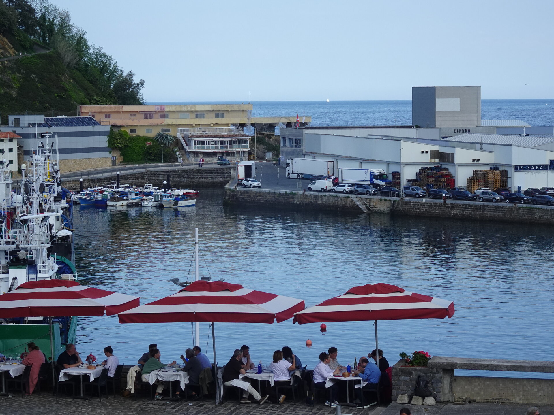 Diners under red-striped umbrellas beside the harbour at dusk
