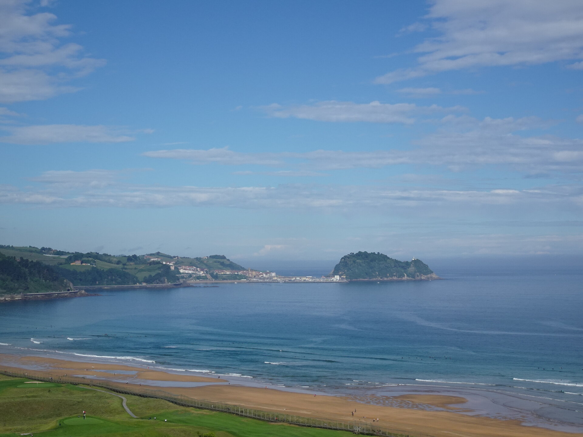 View across a bay to a wooded headland, seaside town and sandy beach