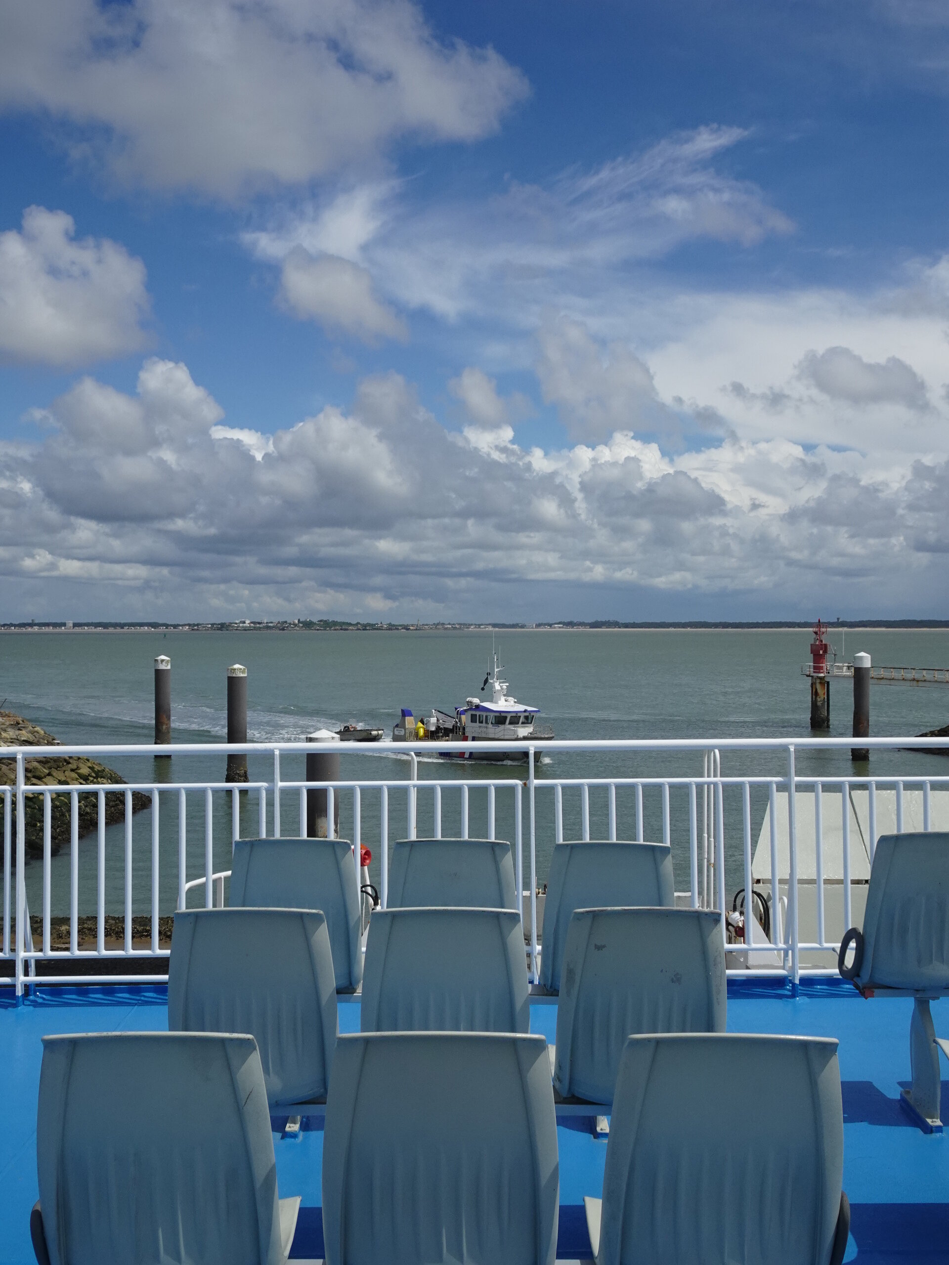 Empty deck chairs on a ferry looking out to a small boat in the harbour