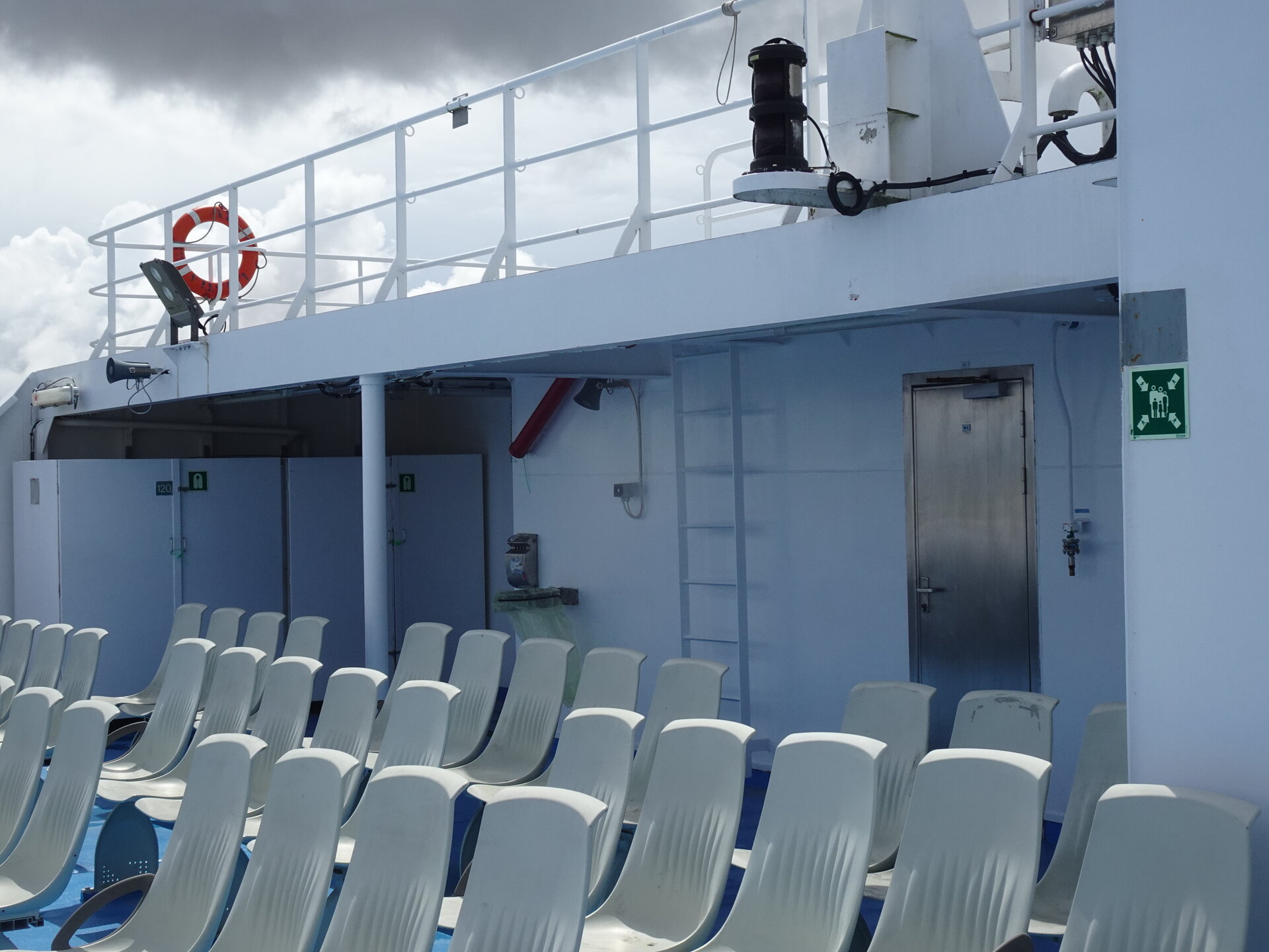 Rows of white plastic chairs on an open ferry deck under a cloudy sky