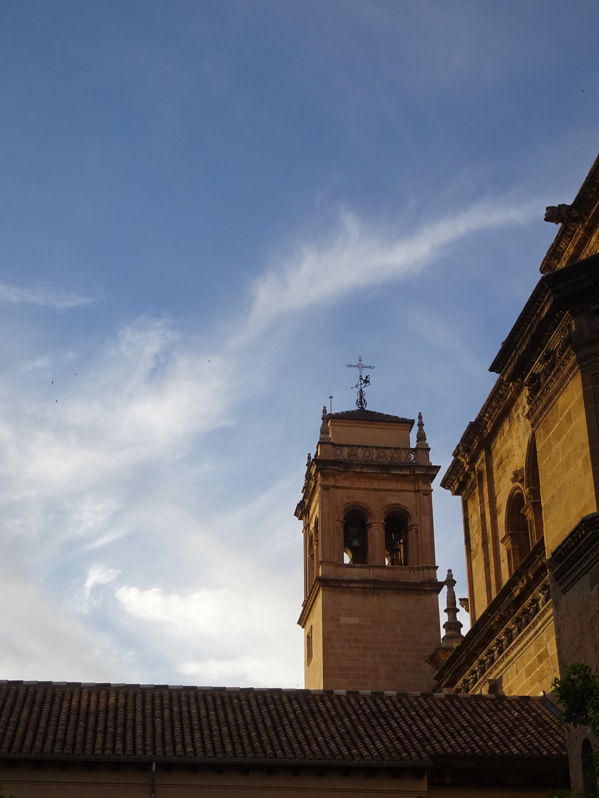 Sandstone bell tower topped with a wrought iron cross against an evening sky
