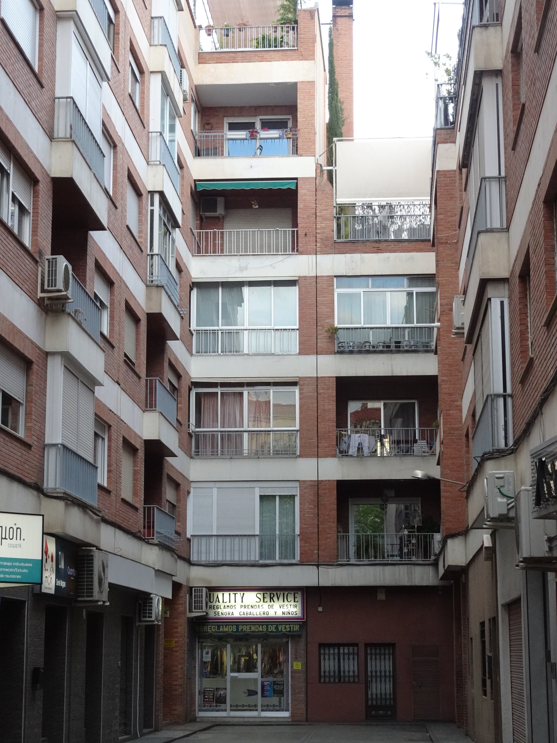 Tall apartment block with stacked balconies and a corner shop at street level