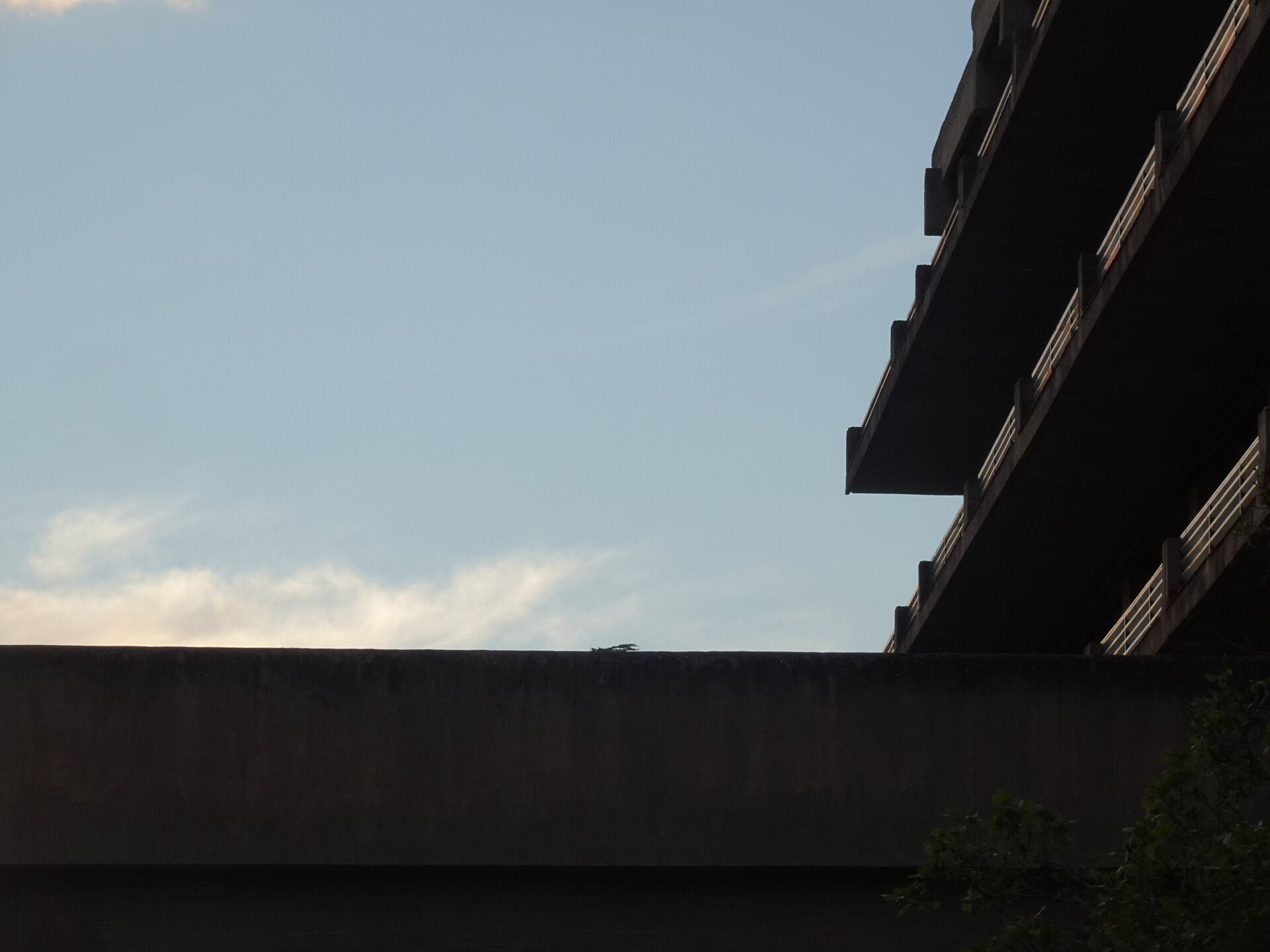 Concrete underside of a stacked balcony block silhouetted against dusk sky