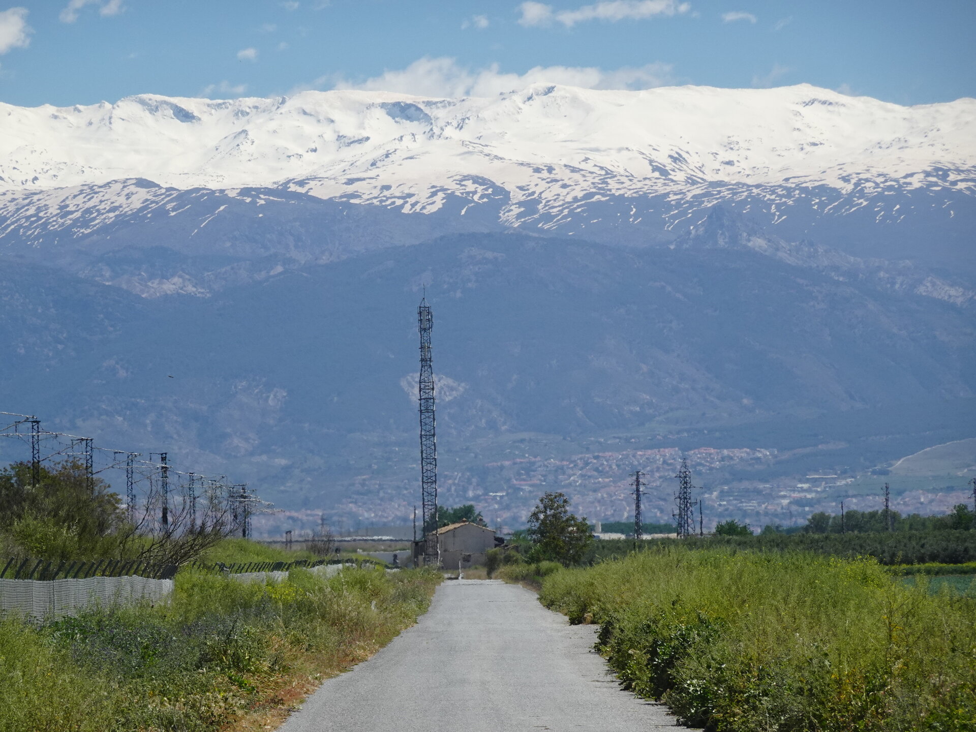 Country lane leading toward the snow capped Sierra Nevada with a tall lattice mast