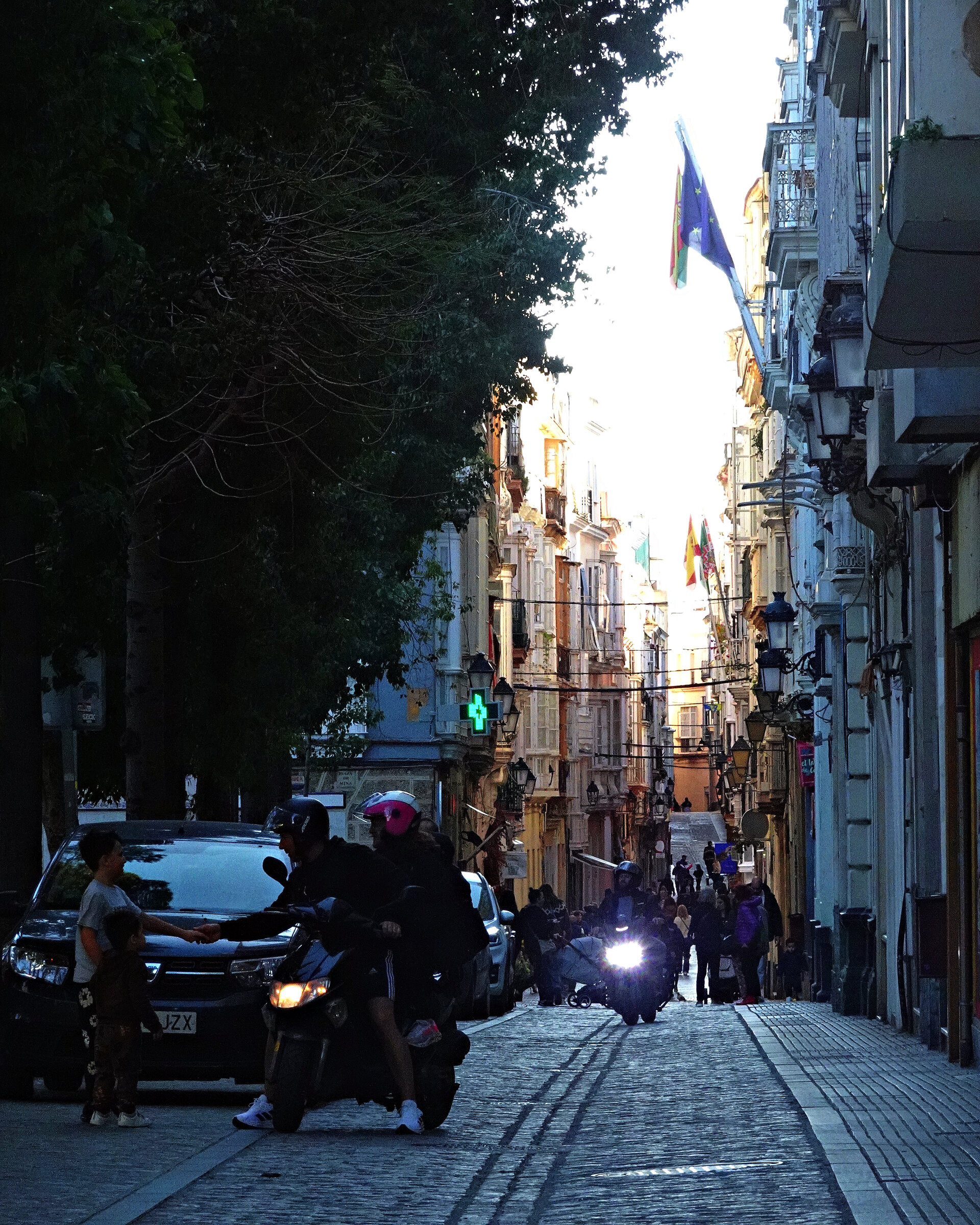 A dark car on a narrow shaded street between tall city buildings