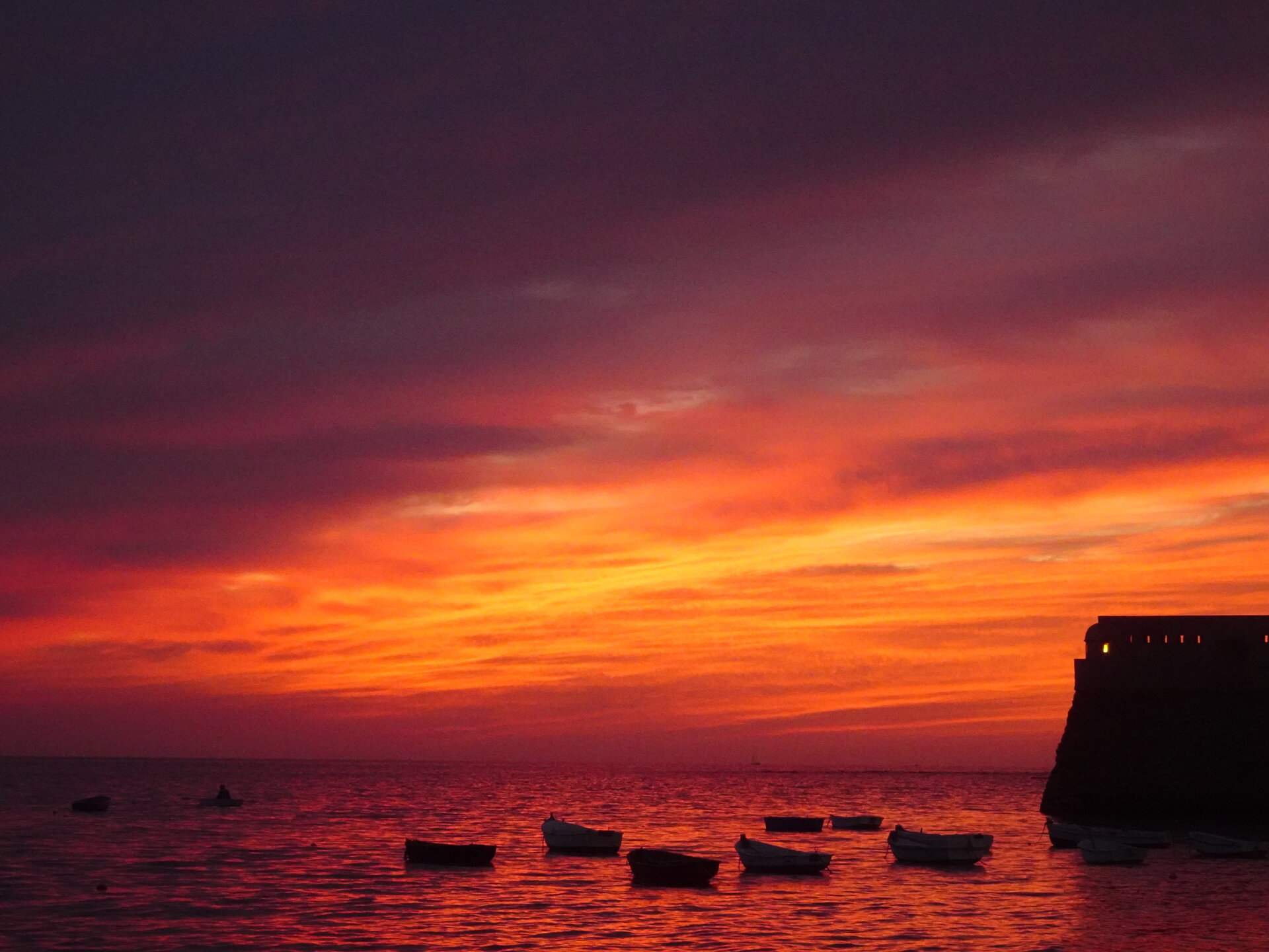 Orange sunset clouds over a dark sea with distant boats