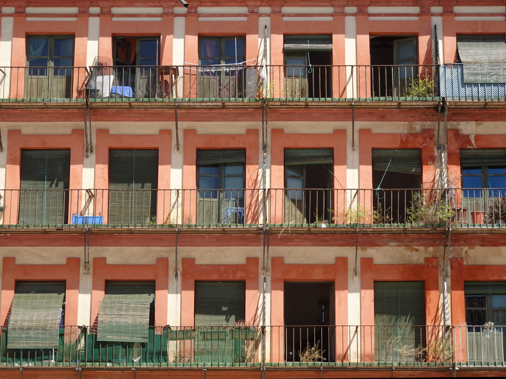 A weathered terracotta apartment facade with plant-filled balconies
