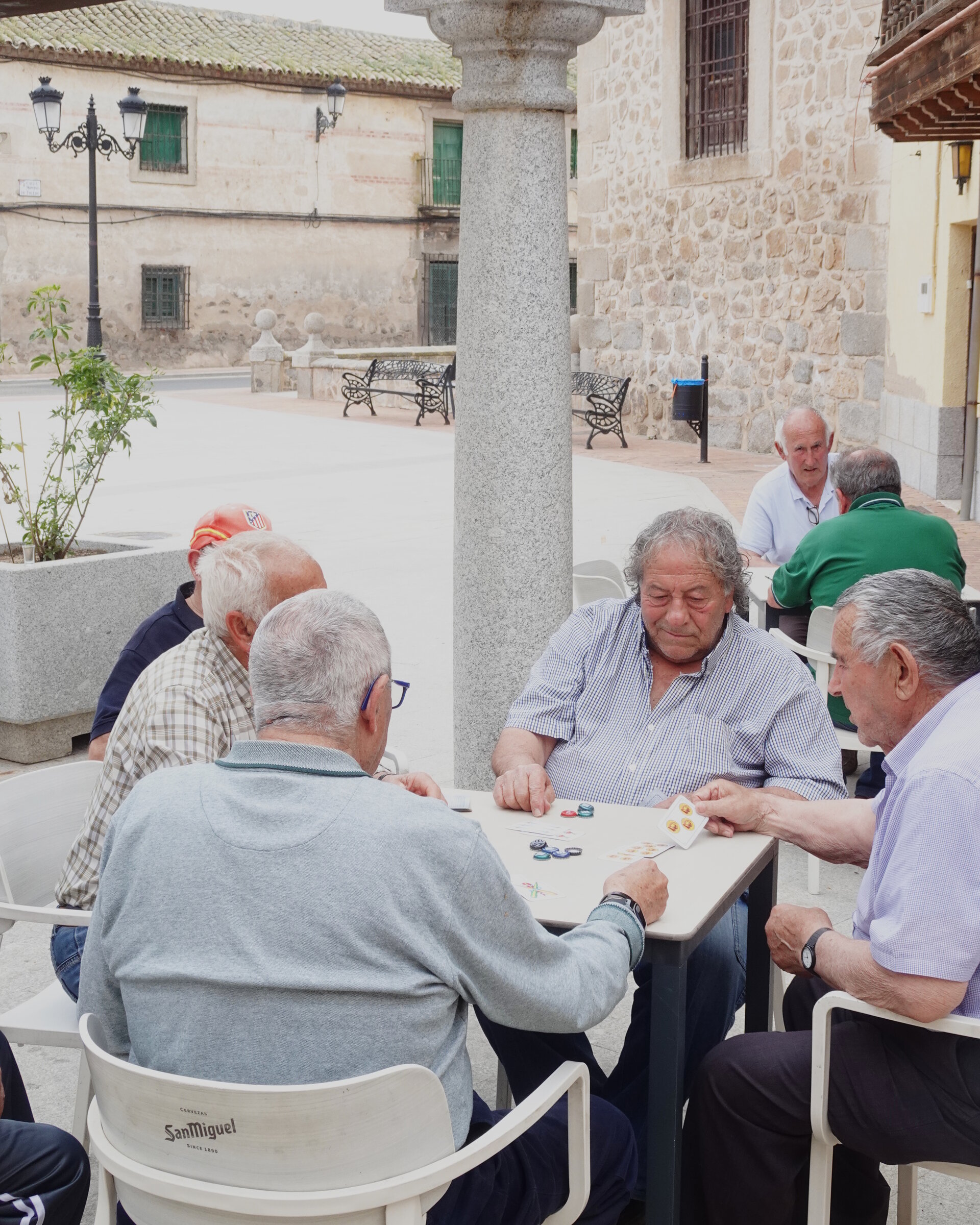 Older men playing cards at a table in a village plaza