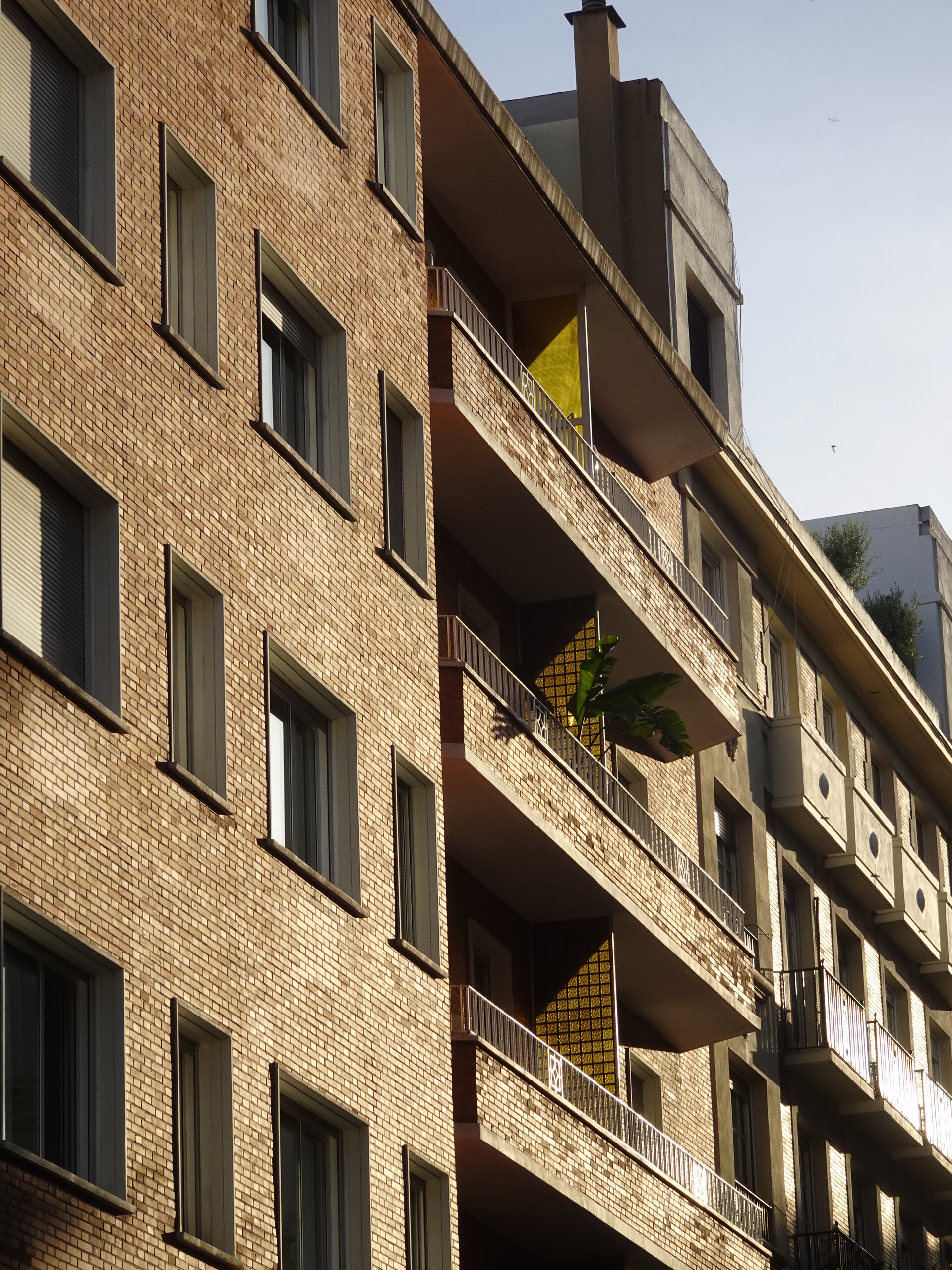 Sunlit brick apartment balconies with a bright yellow panel